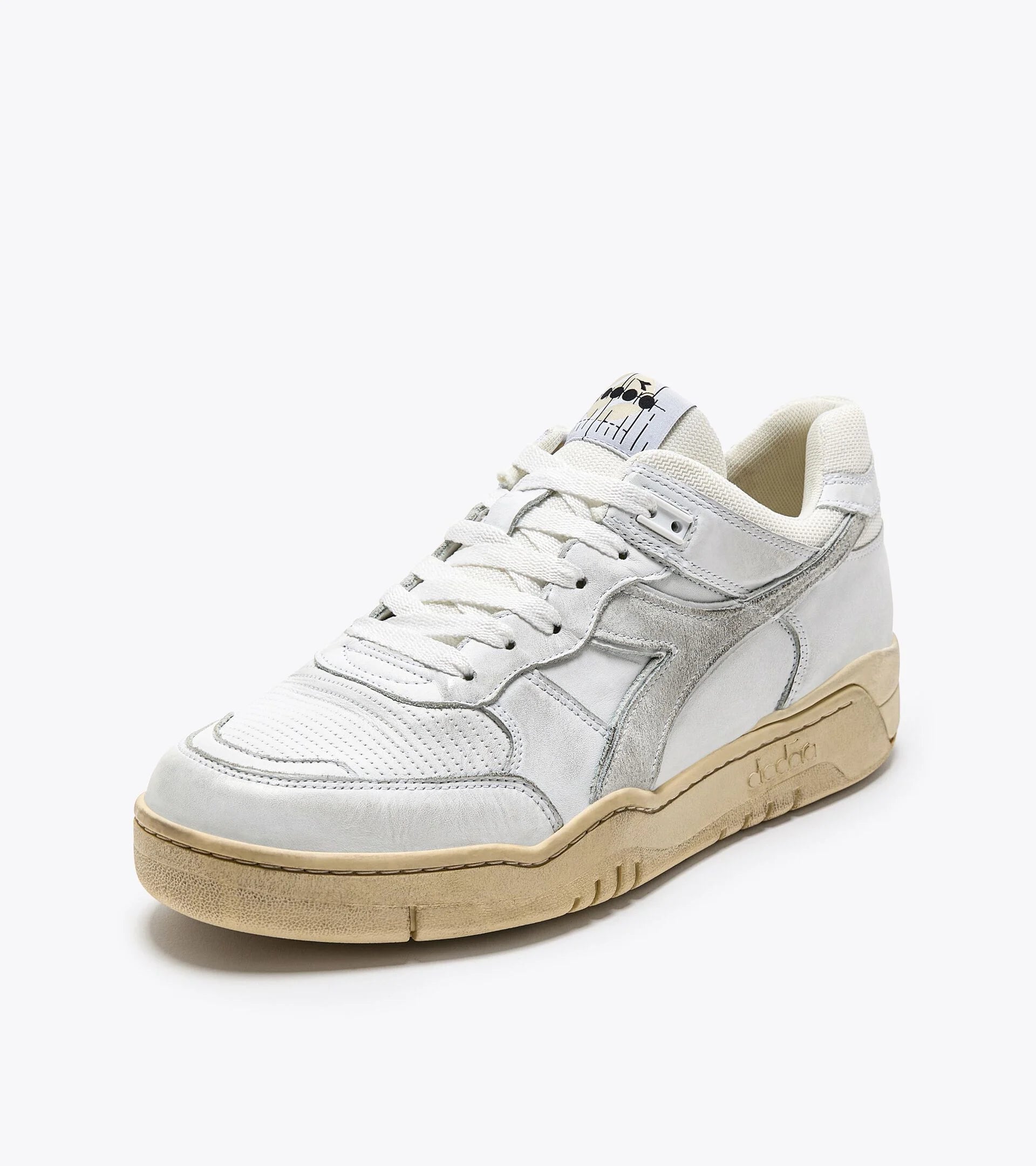 A white Ace Rivington Diadora B. 560 USED sneaker with a vintage design shoe features a white leather upper with grey suede accents, a perforated toe box, and a beige rubber sole. The Diadora logo is visible on the side, and the tongue has a branded label. The sneaker has a worn-in look, giving it a retro aesthetic.