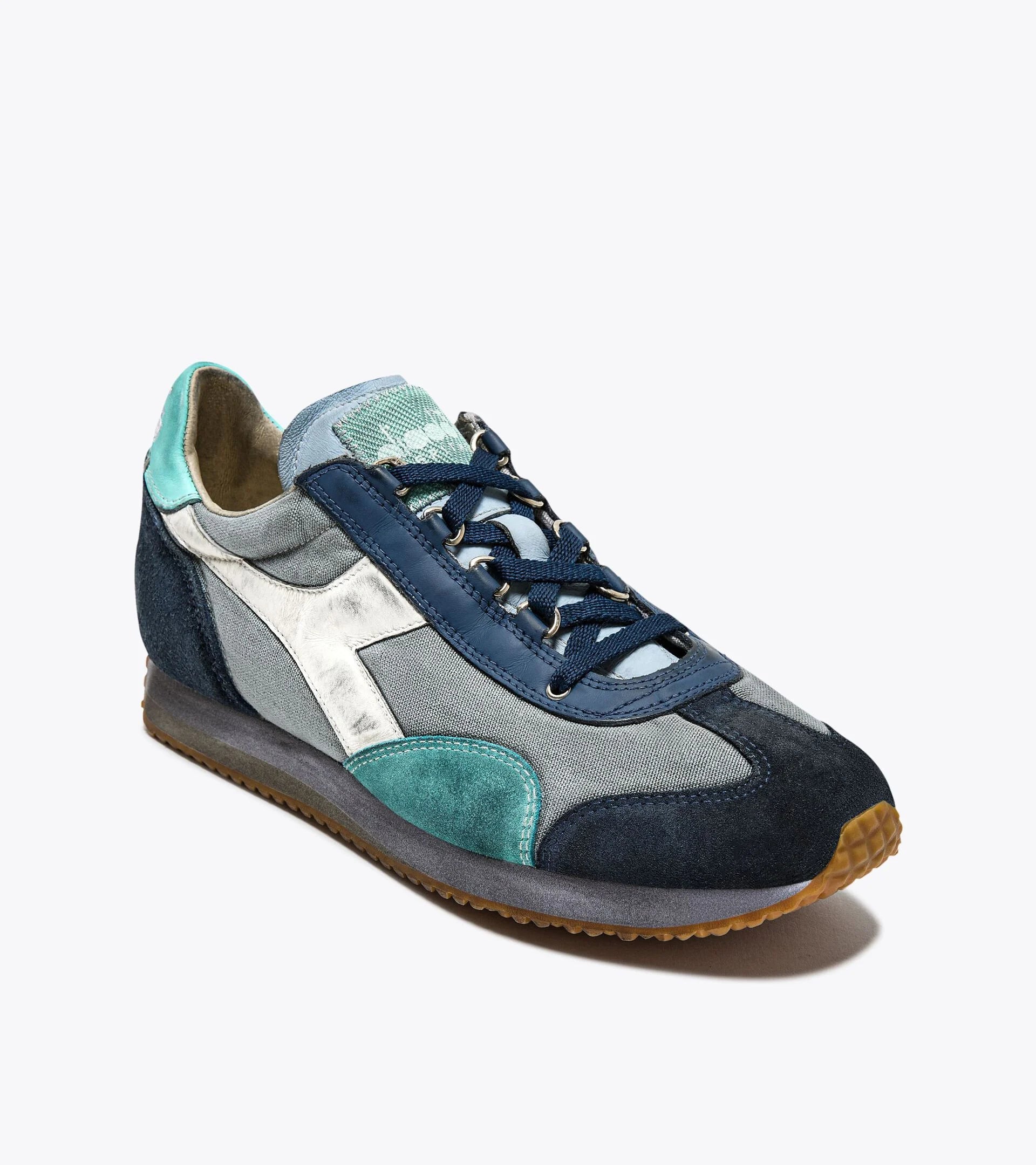 A right-pair upper side view of the Ace Rivington Diadora's Equipe Dirty SW EVO collection in Light Sky Blue features a mix of materials, including denim and suede, with a combination of light blue, dark blue, and teal colors. The design includes a white side stripe, navy blue laces, and a gum sole, creating a retro yet modern look.