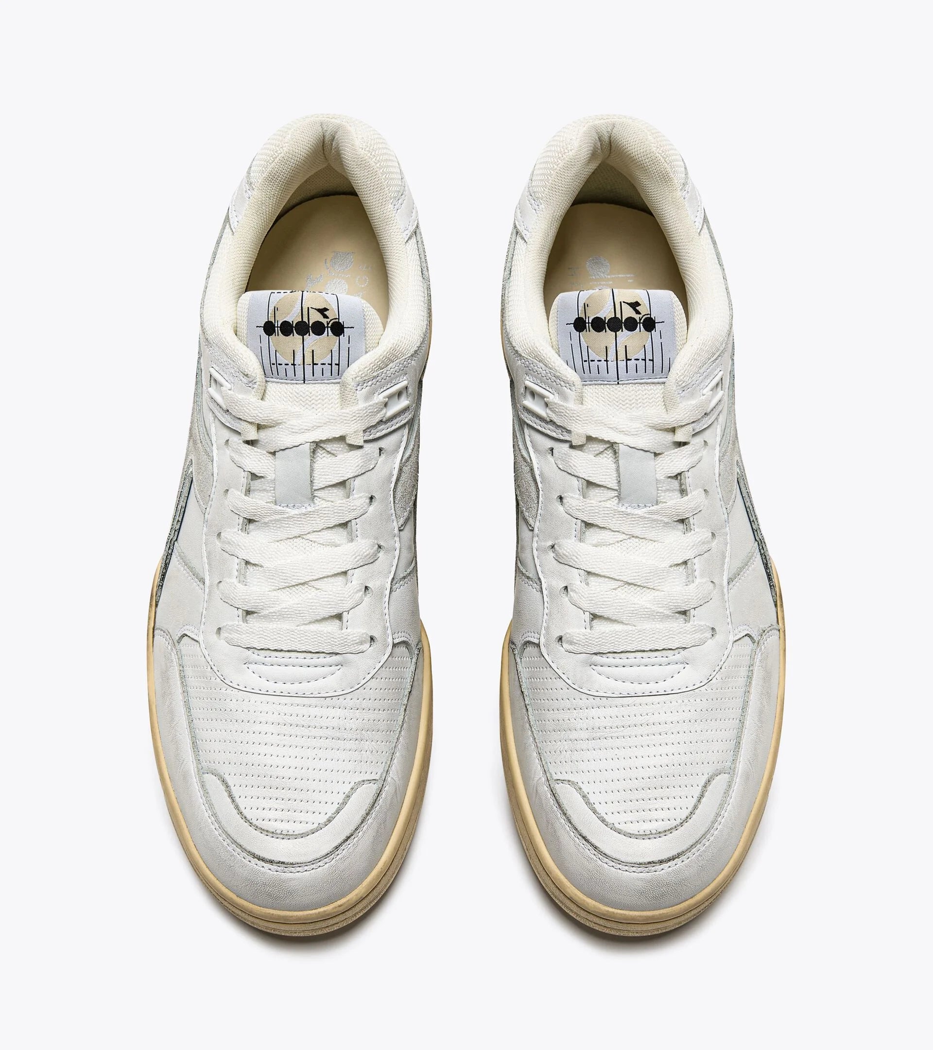 Top view of a pair of Ace Rivington Diadora B. 560 USED sneakers in white shoes features white laces, perforated toe boxes, and a beige inner lining. The insoles display a unique design with black dots and vertical lines. The sneakers have a vintage aesthetic with slightly worn details and a beige outsole.