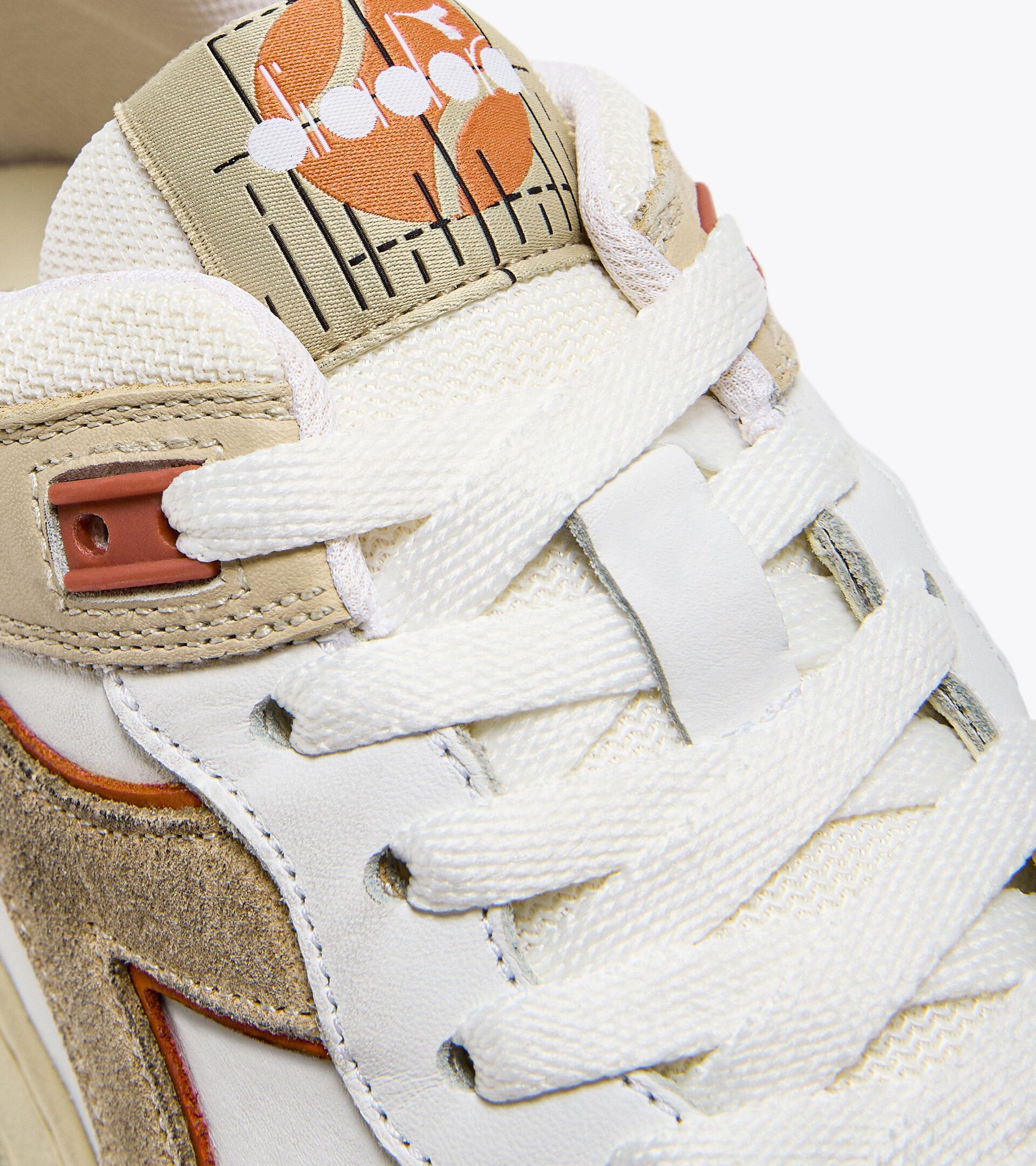 Close-up of the lacing and tongue area of an Ace Rivington Diadora B. 560 USED - Beige Bleached shoe features white laces, beige and tan suede accents, and a distinctive orange and white design on the tongue.