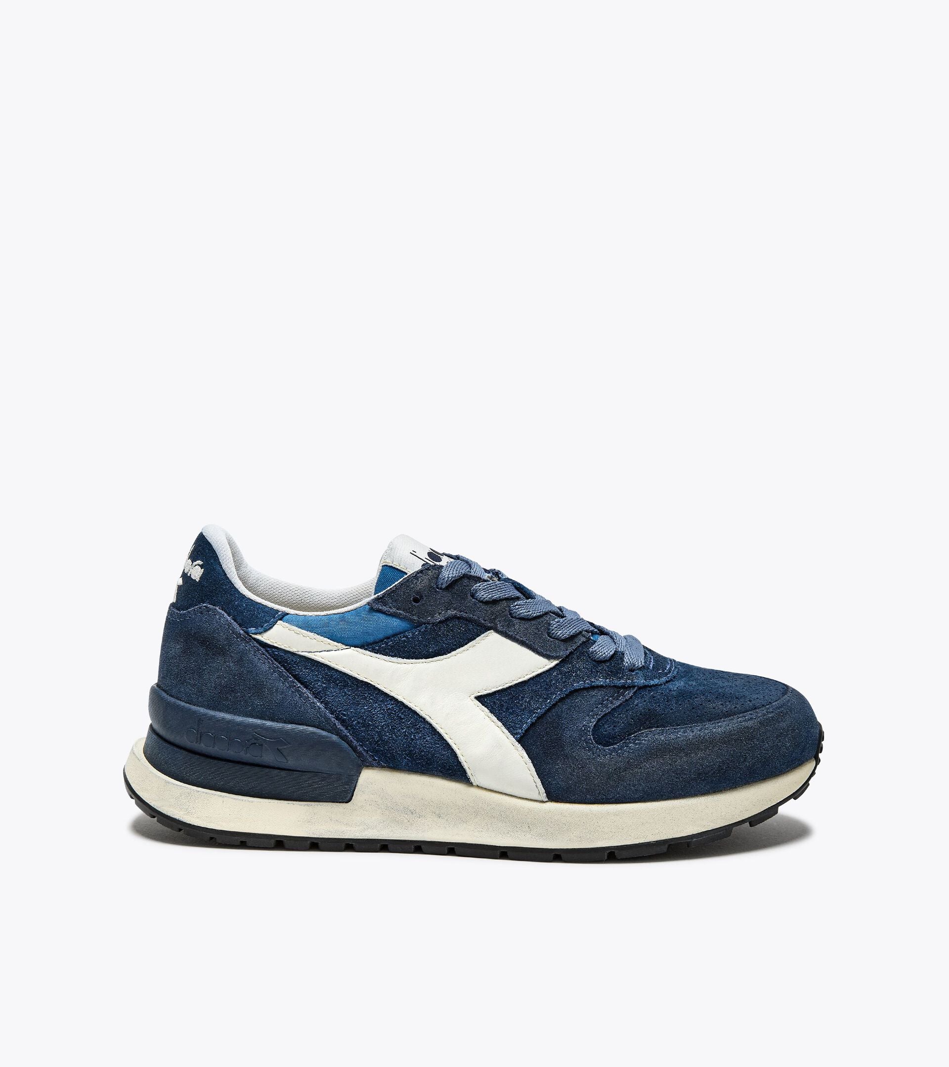 A side view of an Ace Rivington Diadora Conquest Suede SW sneaker in Colonel Blue features a dark blue suede upper with a white leather logo stripe on the side, a white midsole, and a black rubber outsole. The laces and tongue are also blue, and the heel has a textured design for added style.