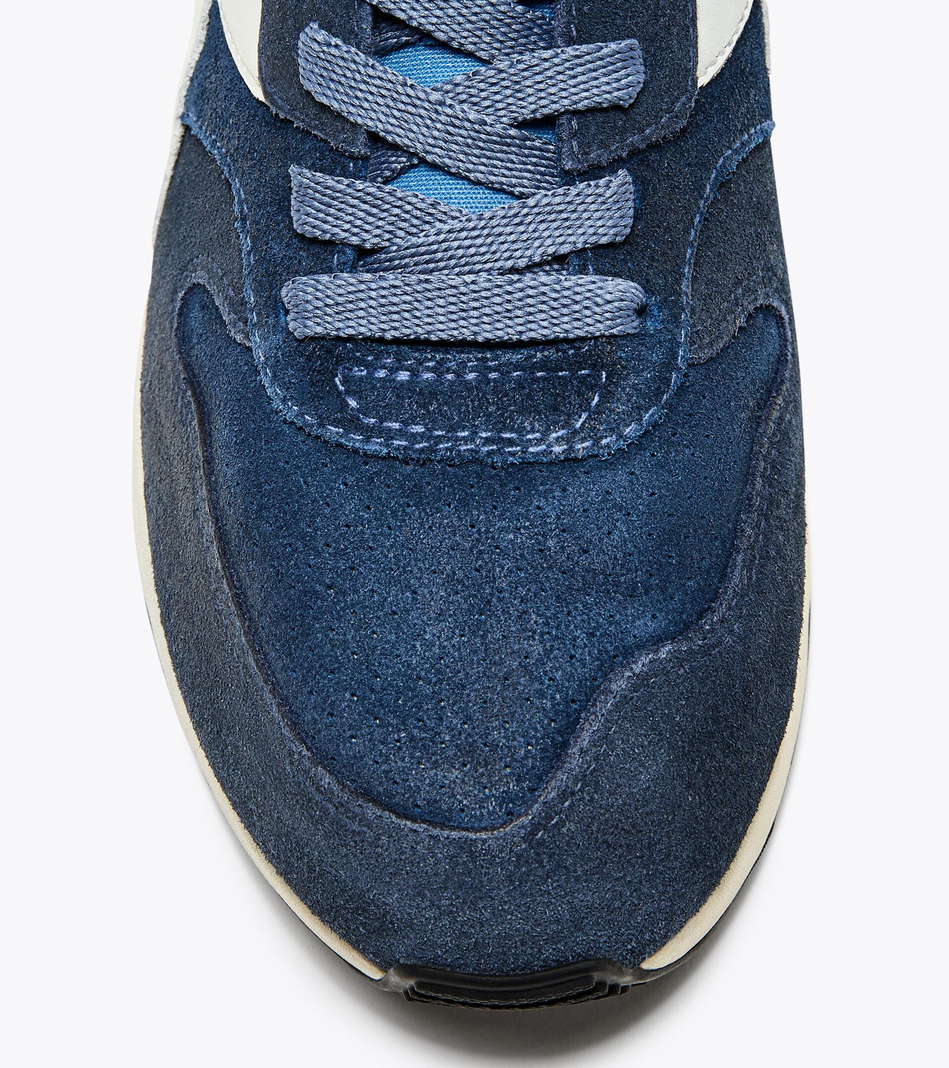 A right-pair close-up top view of the toe area of an Ace Rivington Diadora Conquest Suede SW sneaker in Colonel Blue highlights the dark blue suede material of the upper part of the shoe, with detailed stitching visible. The laces are a lighter blue, and the tongue underneath the laces is also blue. The edge of the white midsole is slightly visible at the bottom of the image.