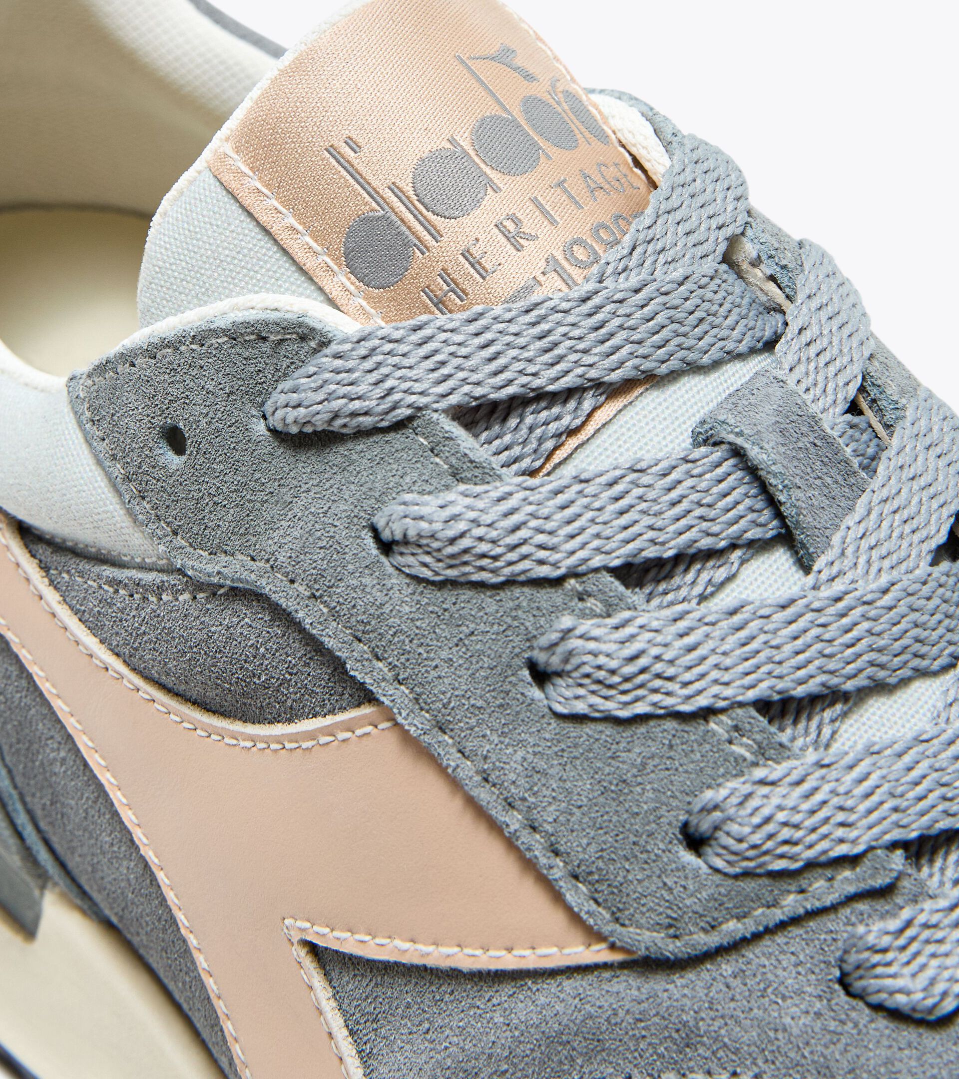 Close-up of an Ace Rivington Diadora Conquest Suede SW - HIgh Rise sneaker, featuring suede material and detailed stitching. The shoe has gray laces and a beige tongue with the Diadora logo and the word 'HERITAGE' printed on it.