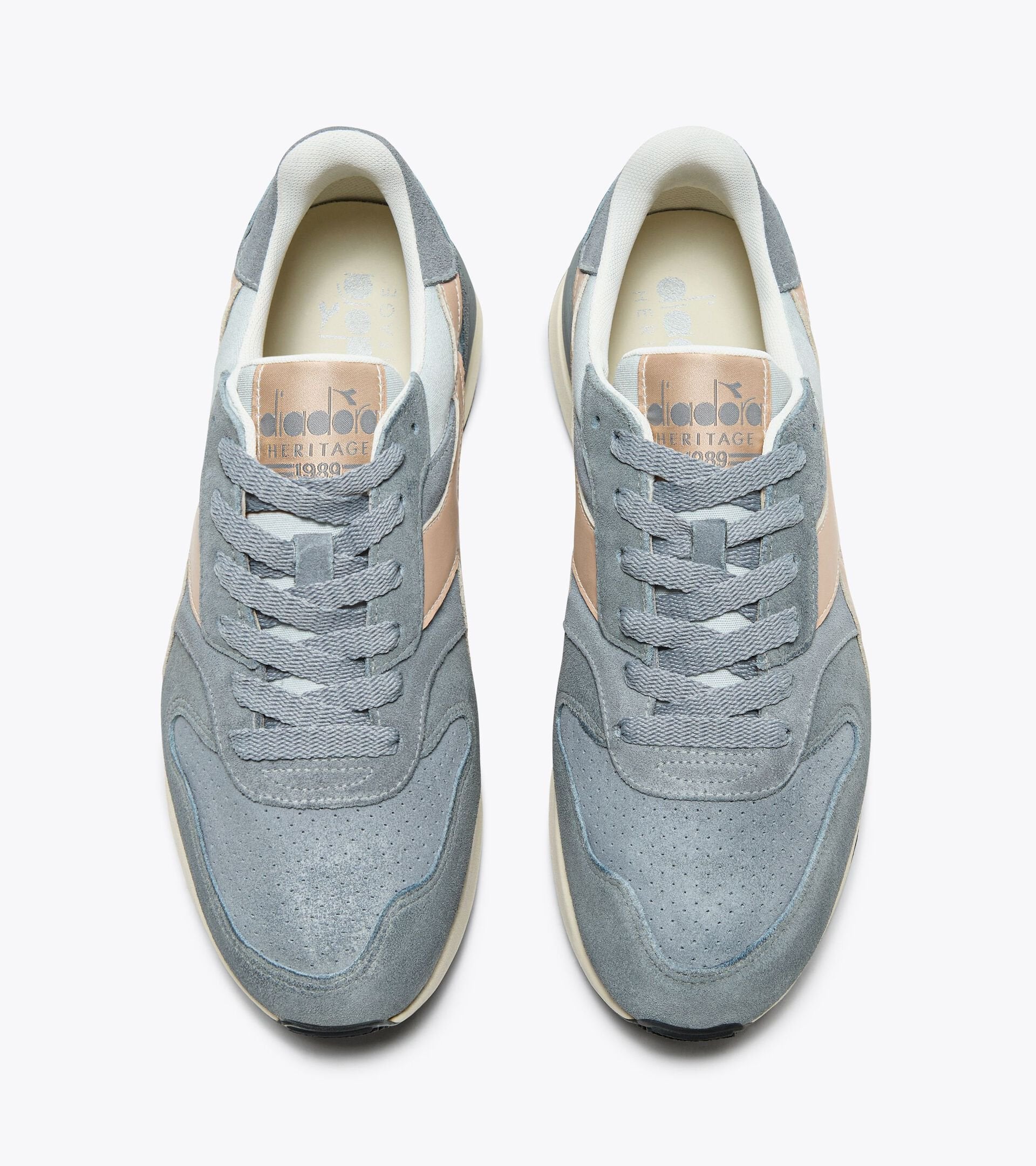 Top view of a pair of Ace Rivington Diadora Conquest Suede SW sneakers in high-rise color shoes features a combination of grey suede and beige leather accents, with grey laces and a beige inner lining. The Diadora logo and 'Heritage' branding are visible on the tongue of each shoe.