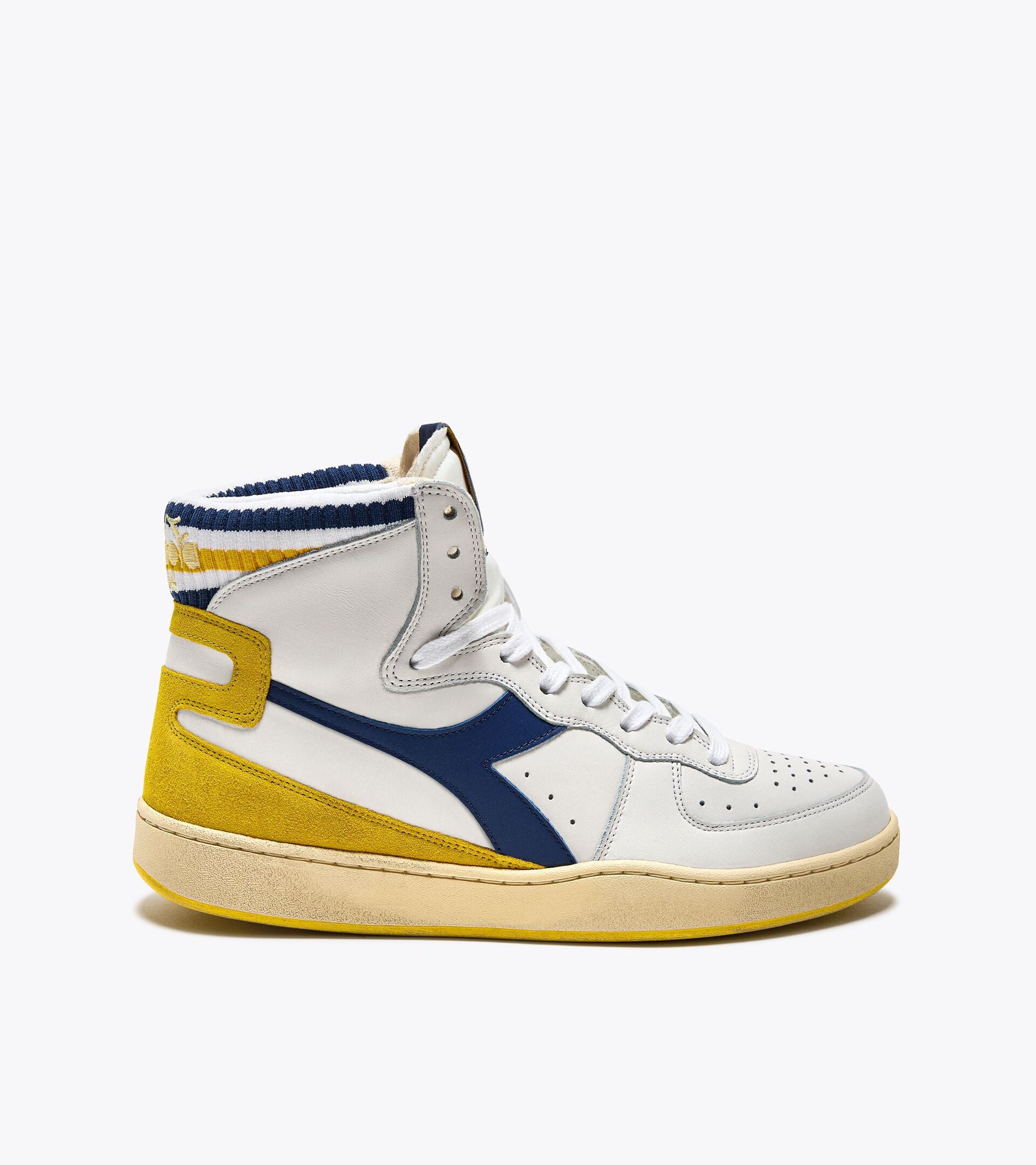 A side view of an Ace Rivington Diadora Mi Basket Forty Knit Italia - White shoe features a high-top design with white leather and yellow suede accents. It has a blue Diadora logo, white laces, and a yellow and blue striped knit collar. The sole is off-white with a slightly worn appearance.