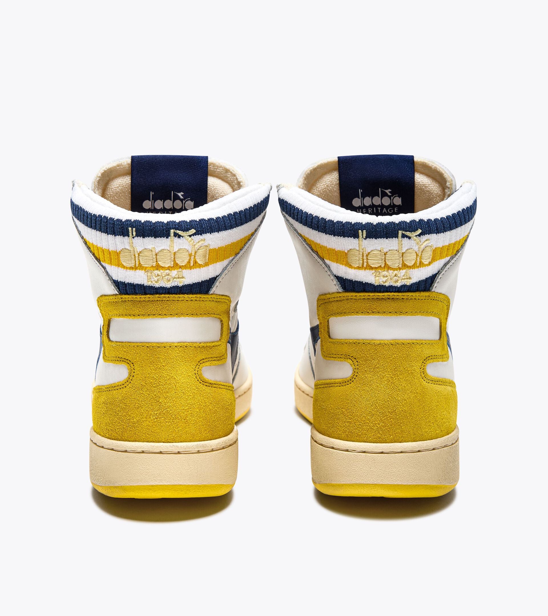 The back view of a pair of Ace Rivington Diadora Mi Basket Forty Knit Italia - White sneakers feature a combination of white, yellow, and blue colors. The heel area is predominantly yellow with a suede texture, and the upper part includes blue and yellow stripes. The Diadora logo is visible on the heel tab, and the sneakers have a high-top design.