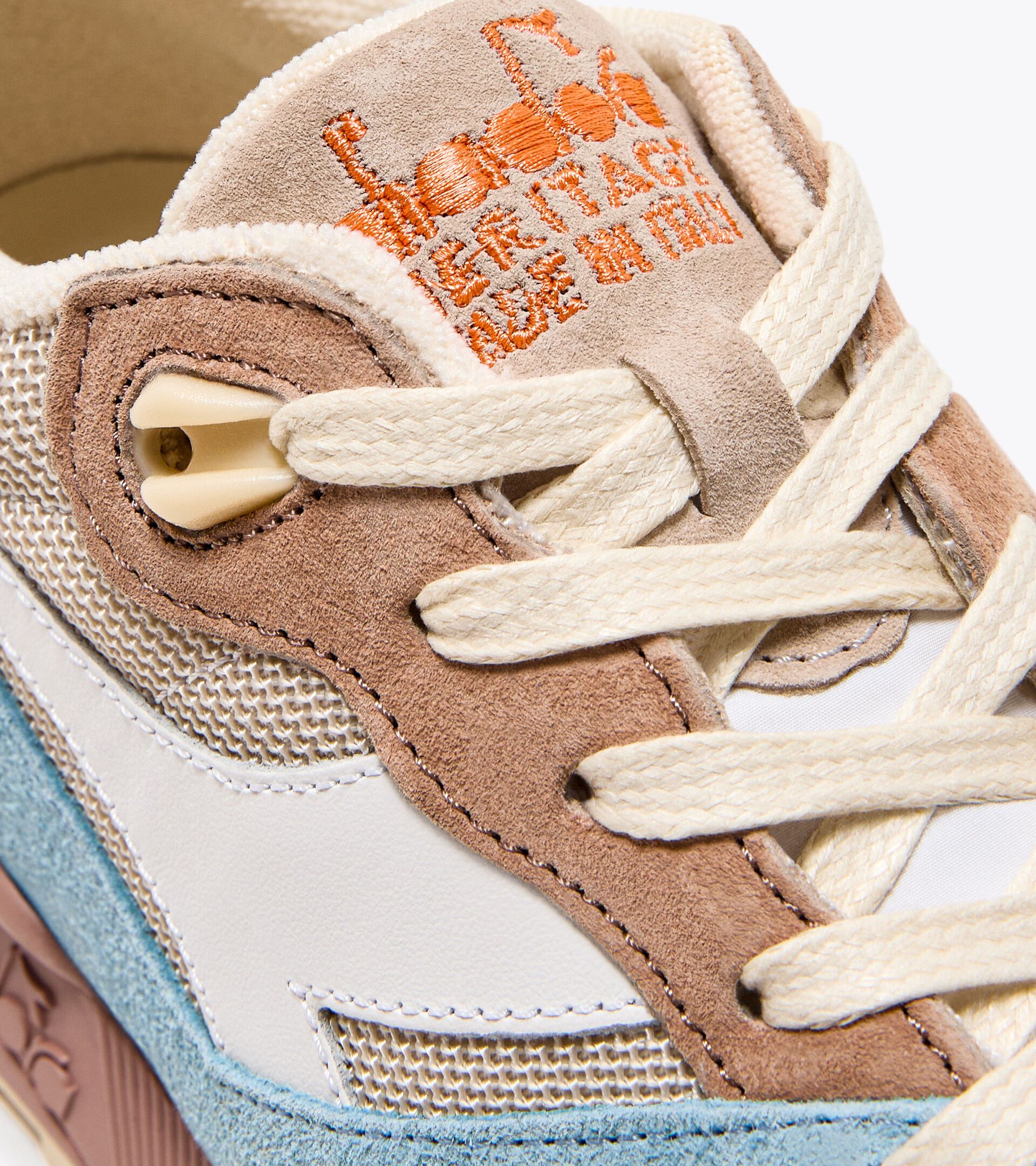 Close-up of the Ace Rivington Diadora - N9000 Tourney Italia - Blue highlights the intricate details of the shoe, including the beige and brown suede overlays, cream-colored laces, and mesh panels. The tongue features embroidered text in orange that reads 'Heritage Made in Italy.' The shoe's craftsmanship and combination of materials are prominently displayed.