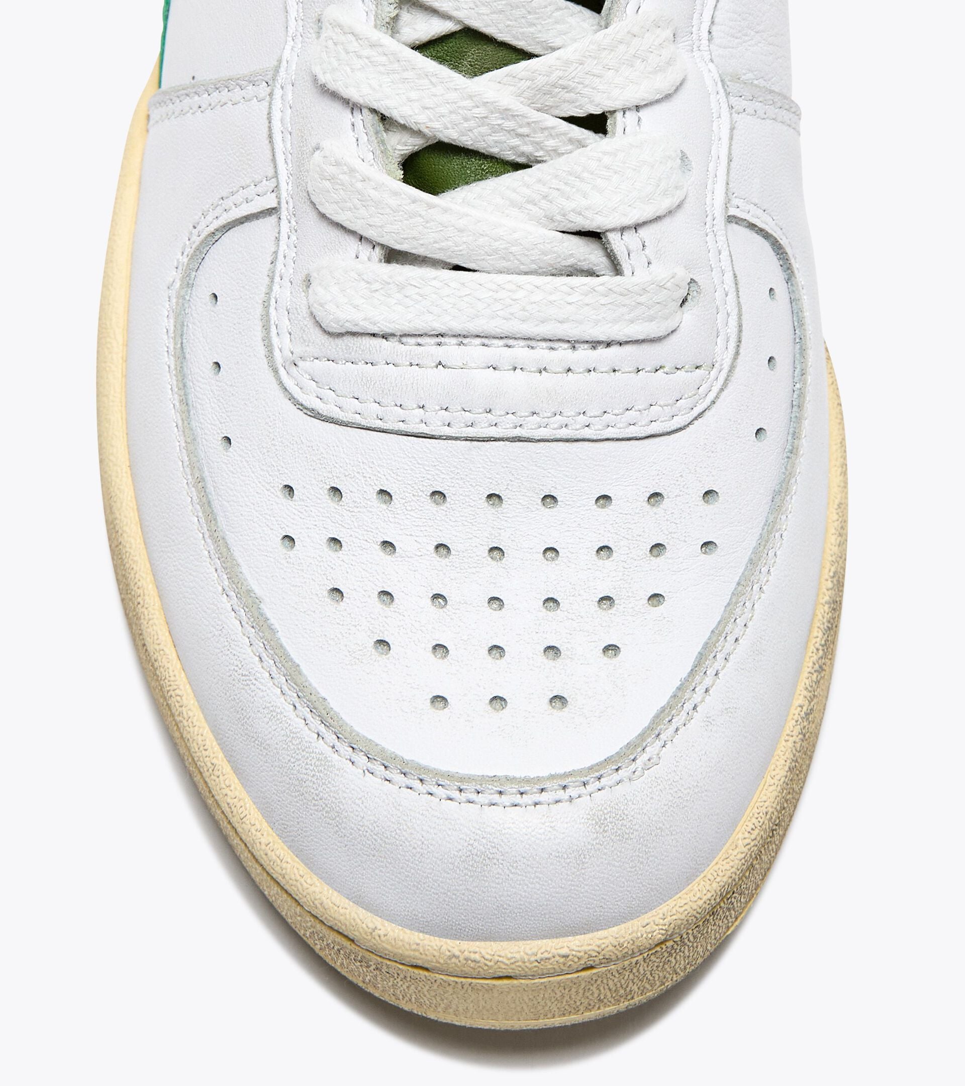 Close-up view of the toe area of an Ace Rivington Diadora - Mi Basket Low Used - White/Pesto shoe features white leather with perforations for breathability, white laces, and a slightly yellowed sole for a vintage look. The green inner lining is partially visible through the laces.