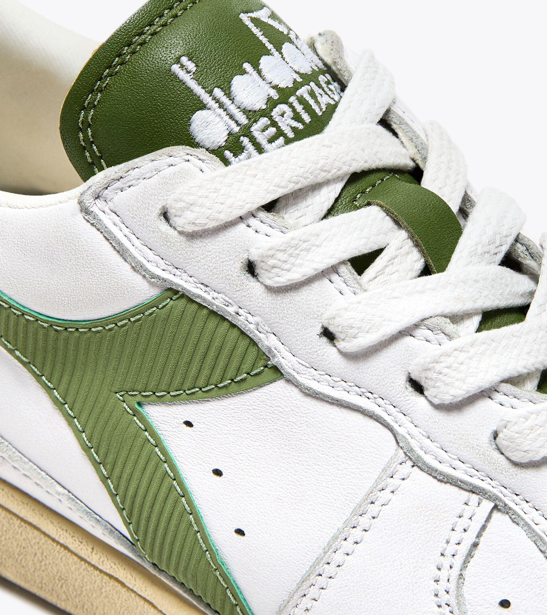 Close-up of an Ace Rivington Diadora - Mi Basket Low Used - White/Pesto features white laces, a green tongue with white embroidered branding, and a green side stripe with ribbed texture. The stitching and material details are visible, highlighting the craftsmanship of the sneaker.