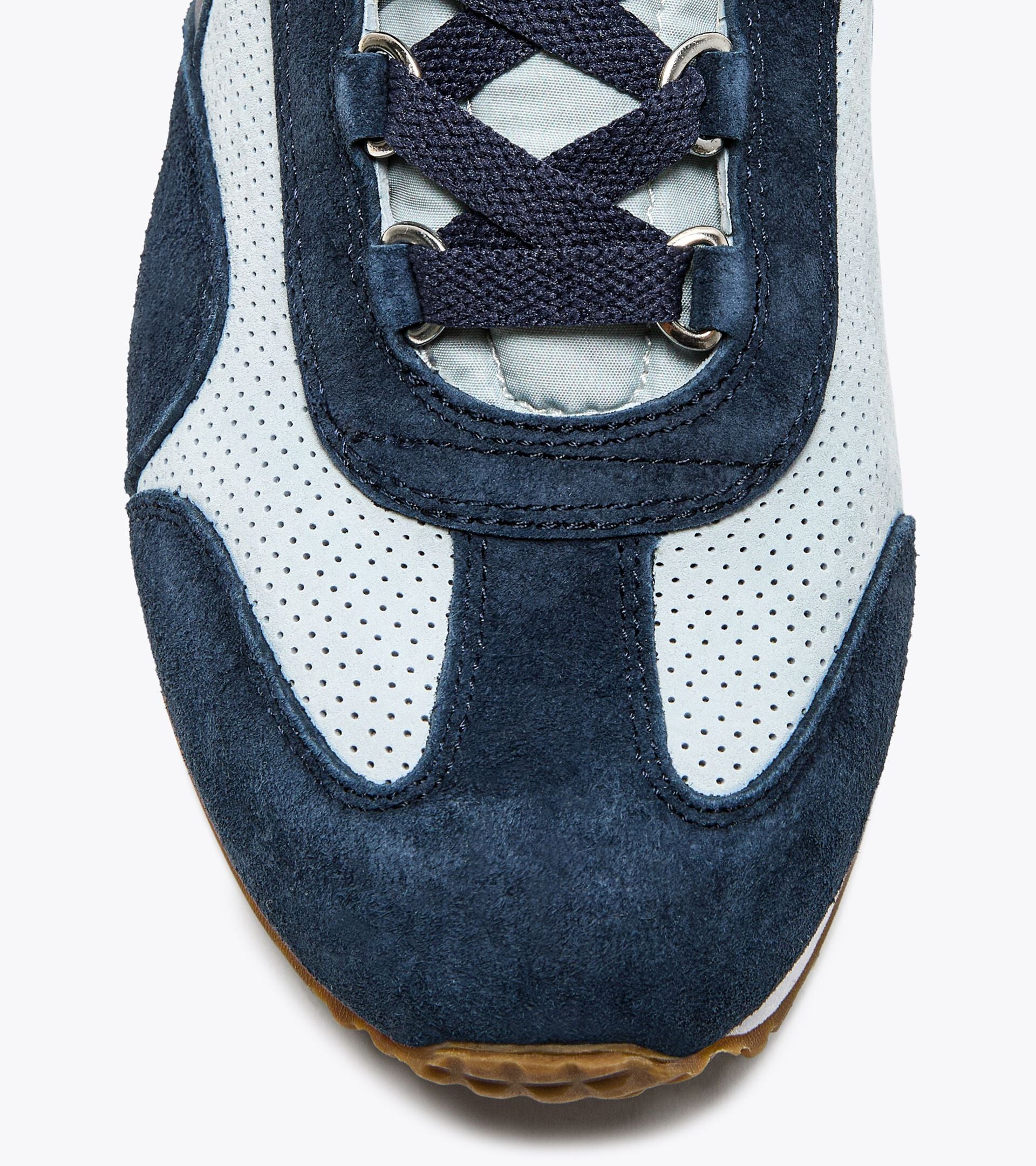 Close-up view of the toe area of an Ace Rivington Diadora Equipe Suede SW sneaker - High Rise shoe features a combination of navy blue suede and light grey perforated leather with navy blue laces. The design includes metal eyelets and a gum sole visible at the bottom edge.