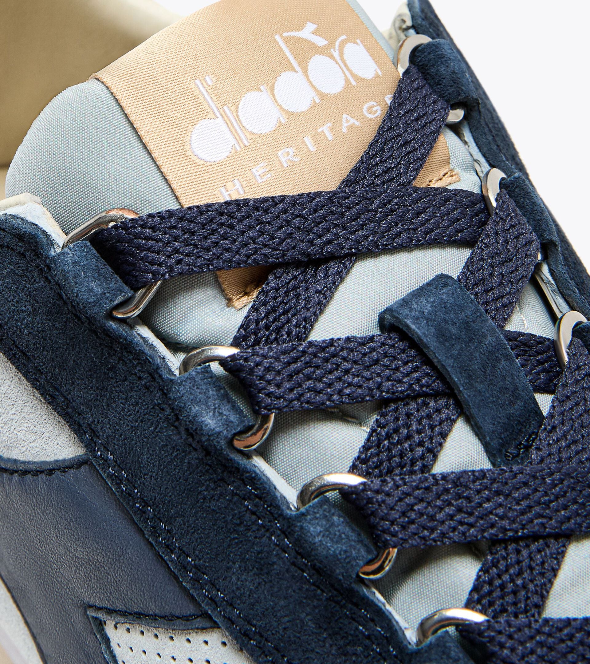 Close-up of the Ace Rivington Diadora Equipe Suede SW - High Rise sneaker, highlighting the intricate navy blue laces, metal eyelets, and the beige tongue label with the Diadora Heritage logo.