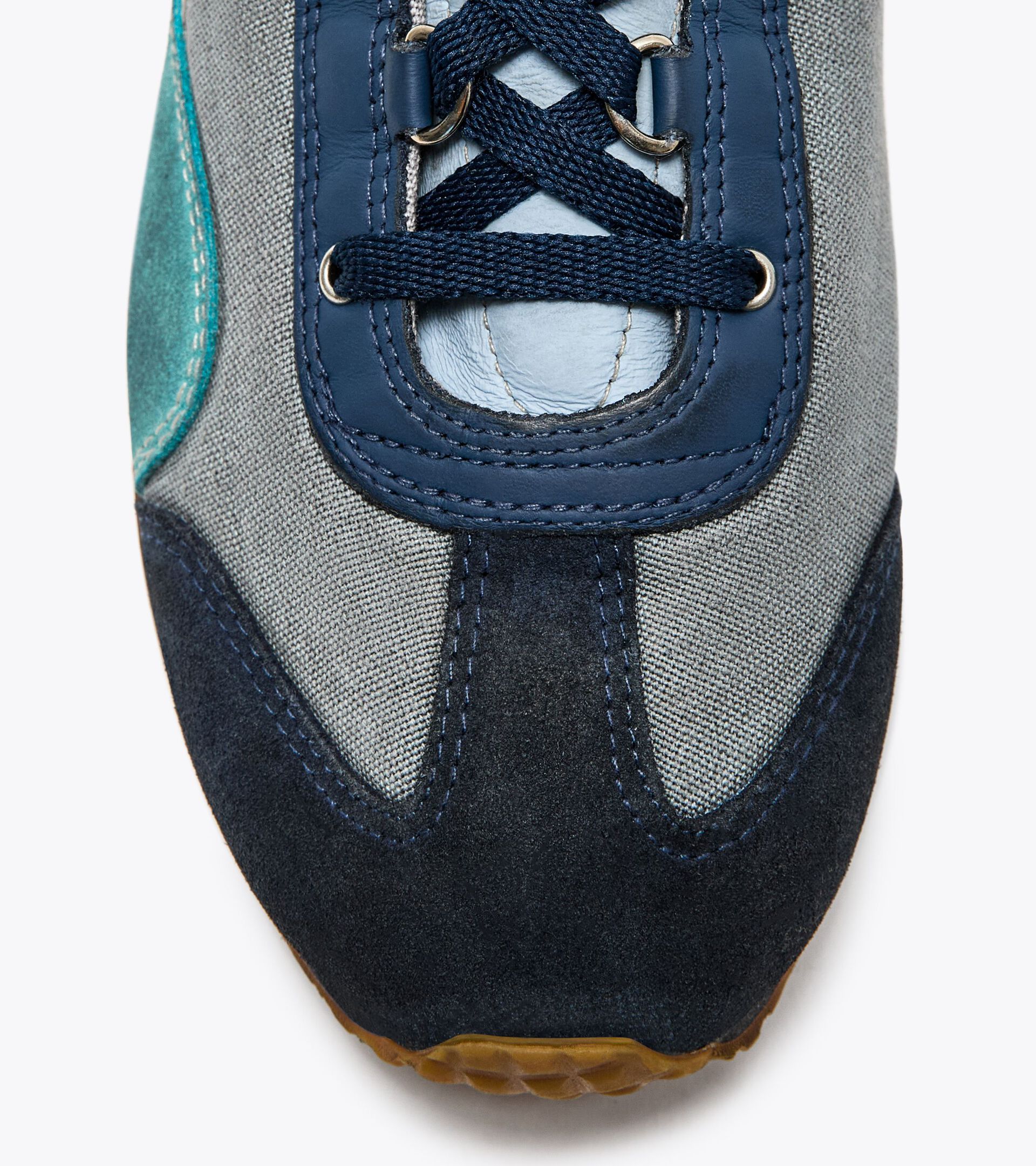 Close-up view of the toe area of an Ace Rivington Diadora - Equipe Dirty SW EVO - Light Sky Blue. The shoe features a combination of materials, including light blue and dark blue suede, grey fabric, and teal accents. The laces are dark blue, and the stitching is visible, adding to the detailed craftsmanship of the sneaker. The sole is partially visible at the bottom of the image.