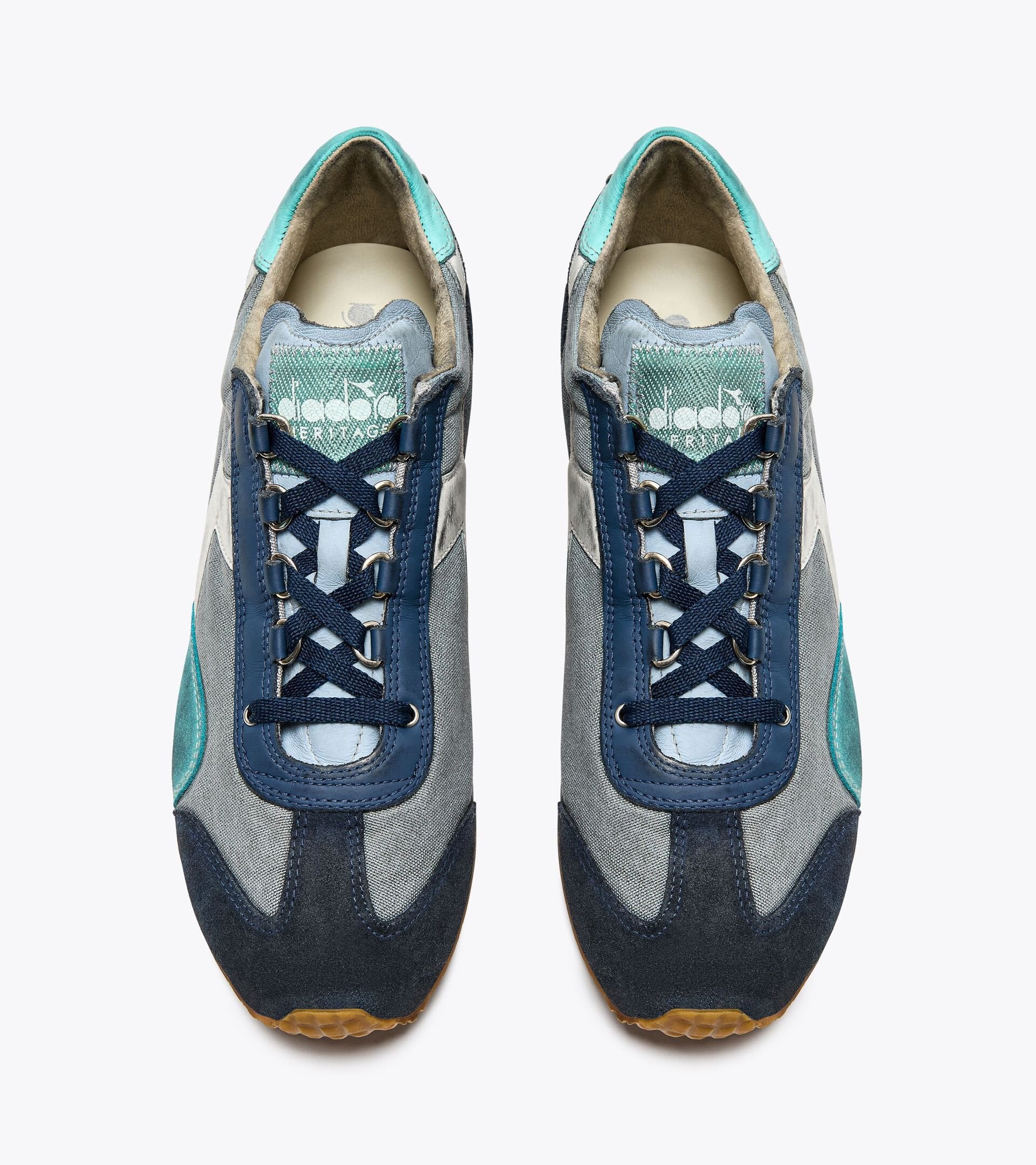 Top view of a pair of Rivington Diadora - Equipe Dirty SW EVO - Light Sky Blue features a combination of blue, grey, and teal colors with dark blue laces. The tongue of each shoe displays the Diadora logo in white on a green background.