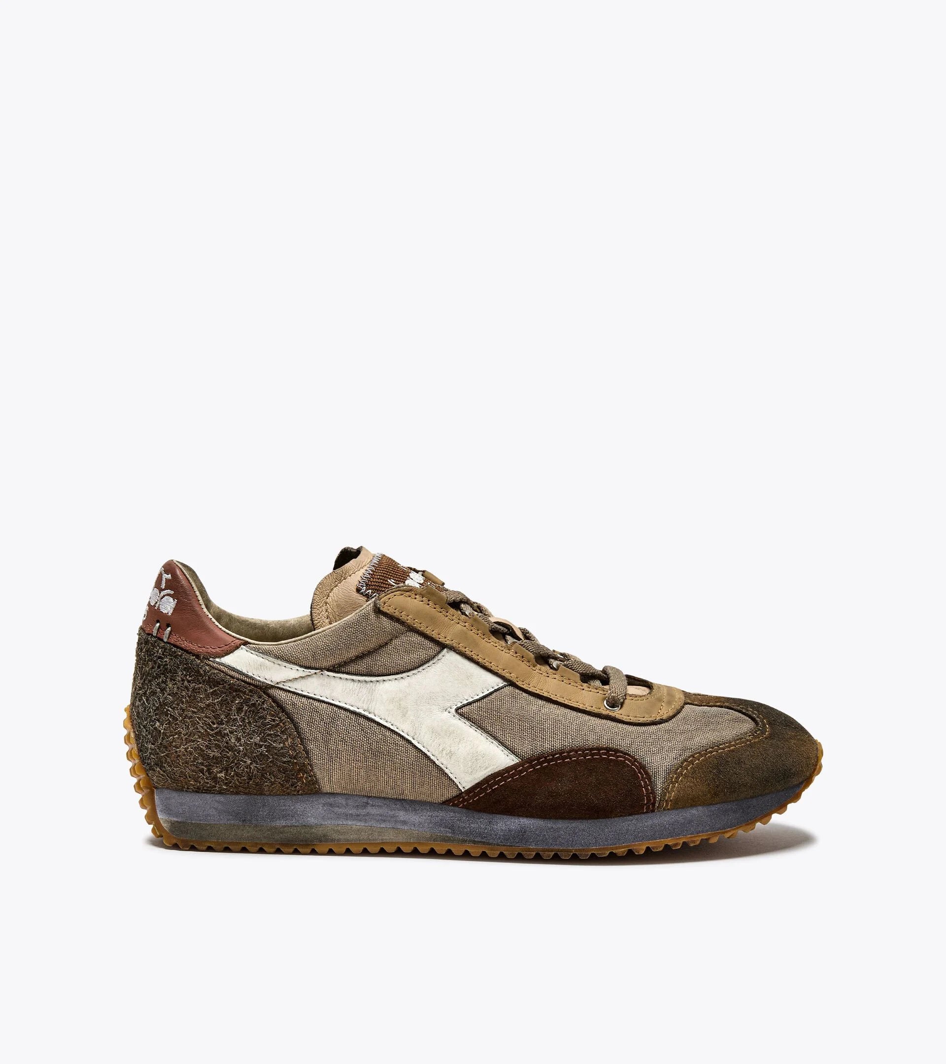 A right-pair side view of an Ace Rivington Diadora - Equipe Dirty SW sneaker in Cuban Sand features a mix of brown, tan, and beige suede and fabric upper with a white leather logo stripe on the side. The sneaker has a textured brown heel, a grey midsole, and a gum rubber outsole with a ridged pattern for traction. The laces are brown, and the tongue is made of a similar tan fabric. The heel also has a white logo design for added style.