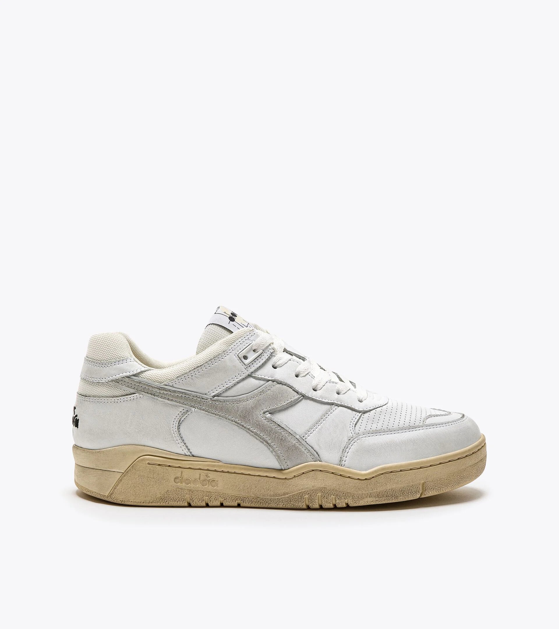 Side view of a white Ace Rivington Diadora B. 560 USED sneaker shoe featuring a suede and leather upper with a slightly worn appearance, a beige rubber sole, and white laces. The Diadora logo is visible on the side, and the shoe has a retro, vintage-inspired design.