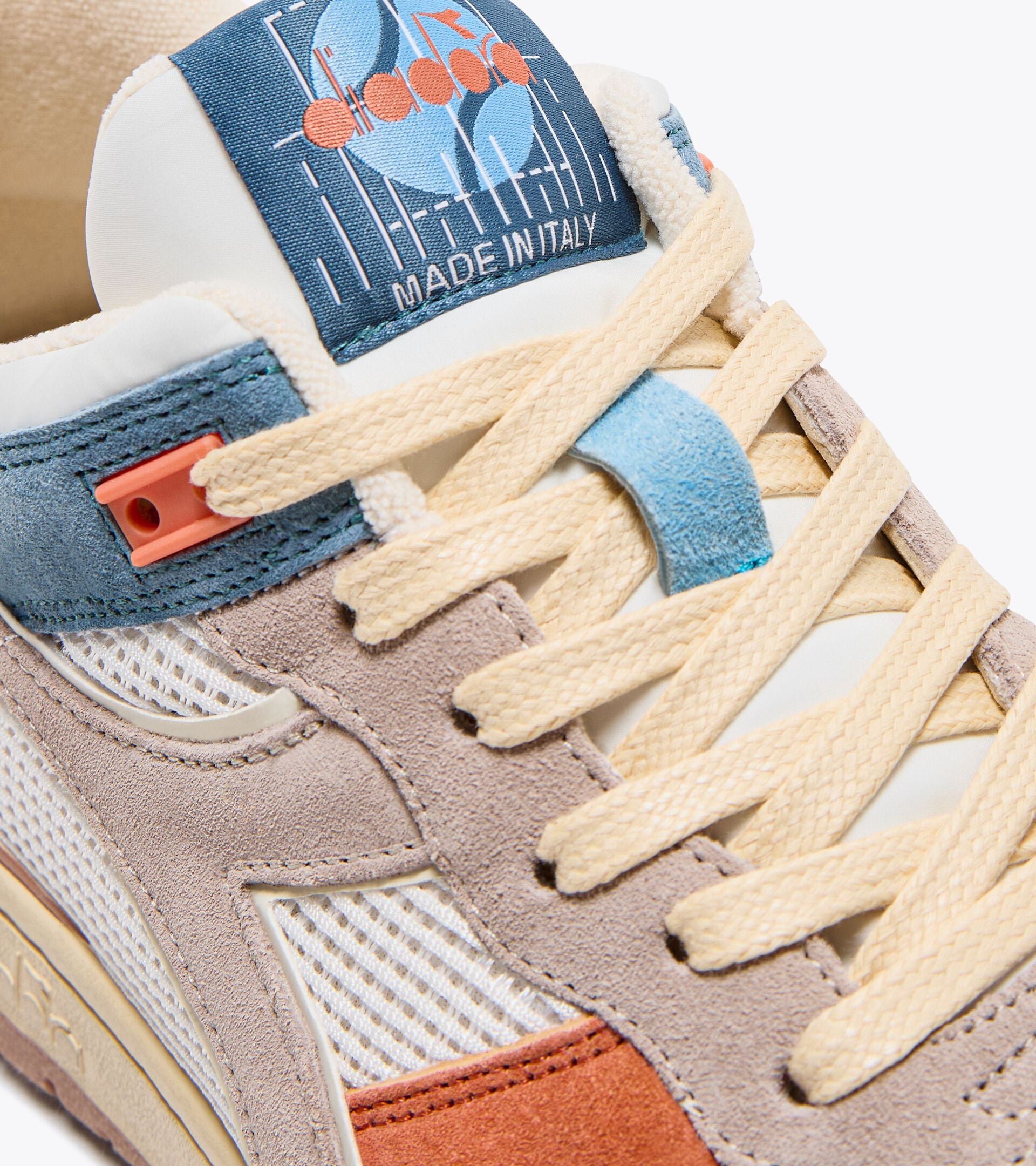 Close-up of the Ace Rivington Diadora B. 560 USED - Tourney Italia sneaker, highlighting the intricate details of the shoe's design. The image shows the shoe's laces, suede, and mesh materials, and a label on the tongue with a graphic and the text 'MADE IN ITALY.' The shoe features a mix of beige, blue, and orange colors, showcasing its high-quality craftsmanship and stylish design.