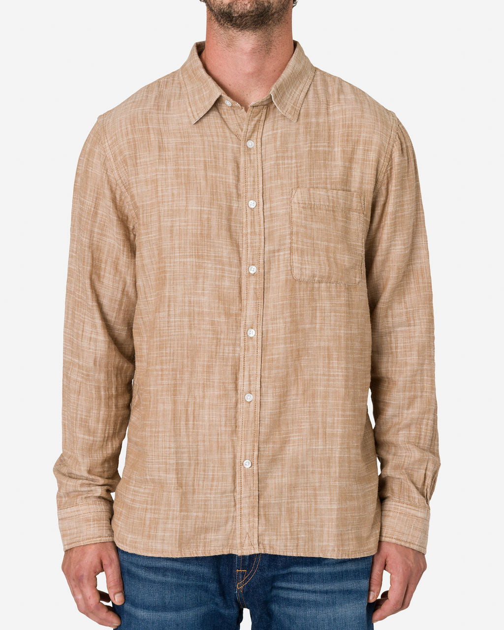 Man wearing a Double Gauze - Long Sleeve - Camel shirt with a subtle checkered pattern paired with denim jeans in the plain white background.