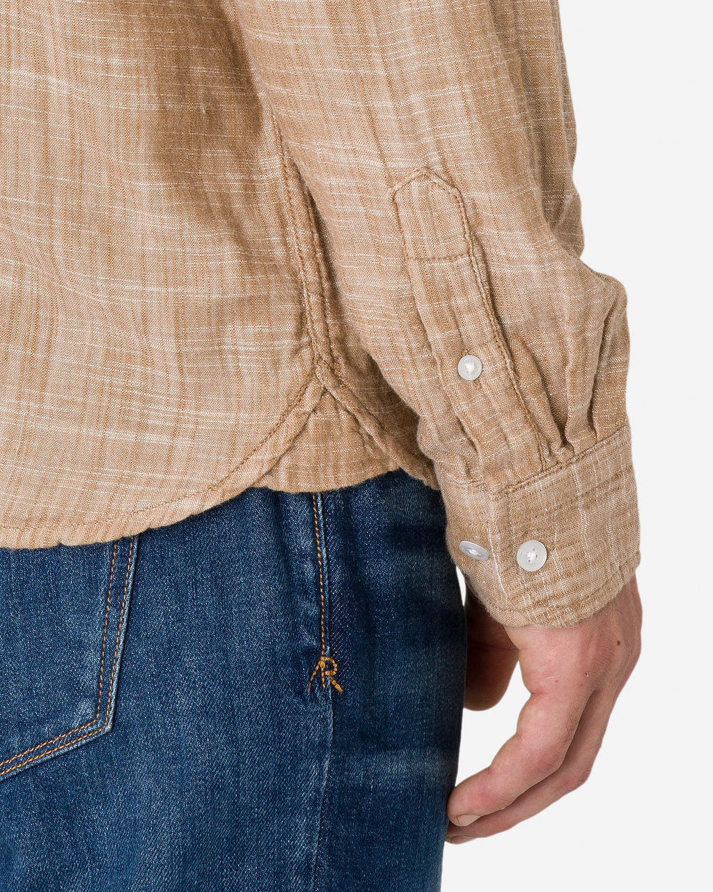 A close-up view of a man's right arm and hand is shown wearing a camel-colored double gauze long-sleeve shirt with a textured pattern and buttoned cuffs by Ace Rivington. The shirt is paired with blue jeans.