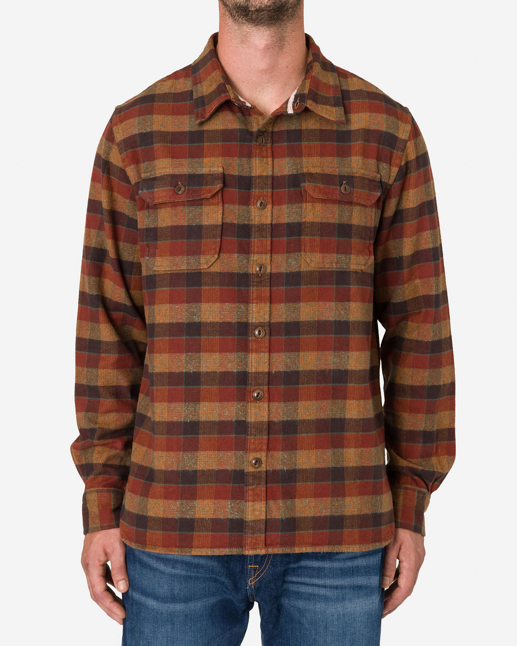 A man is wearing a long-sleeved, button-up flannel utility shirt by Ace Rivington. The shirt features a plaid pattern in clay tile colors, incorporating shades of brown, red, and yellow. It is paired with blue jeans. The design includes two chest pockets with button flaps, which draw attention to the man's upper body, showcasing the shirt's design and fit against a plain white background.