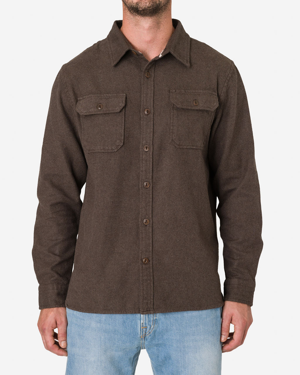 A man wearing a long-sleeve flannel utility shirt - cedar color, which features a collar and two chest pockets, each secured with a buttoned flap paired with light blue jeans. The image focuses on the upper body, highlighting the details of the shirt's design and texture.