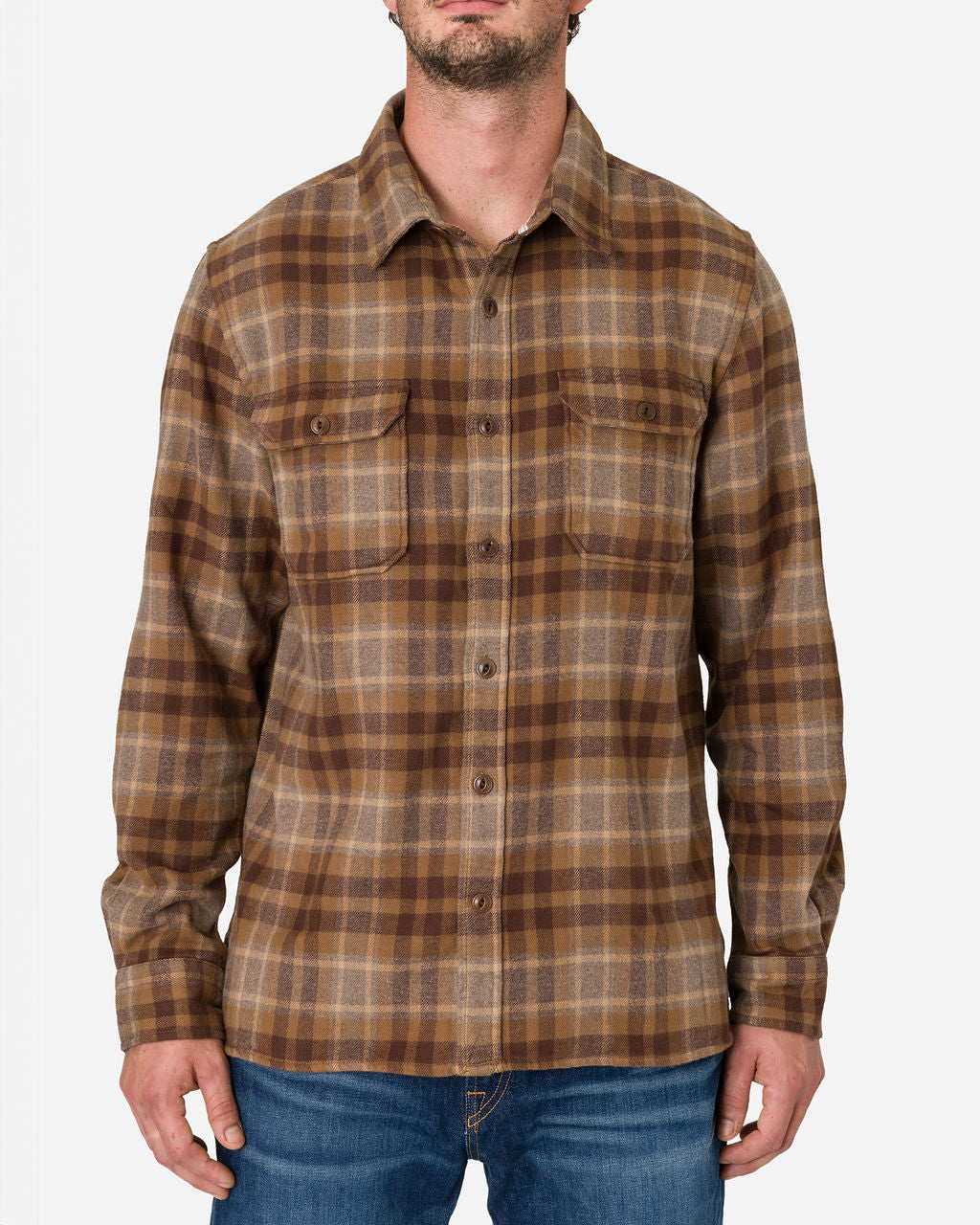 The man is wearing a long-sleeved, button-up Desert Bark flannel Utility shirt with a brown and beige plaid pattern. The shirt has two chest pockets with buttoned flaps paired with blue jeans by Ace Rivington. The image focuses on the upper body, showing the shirt's design and pattern in detail.