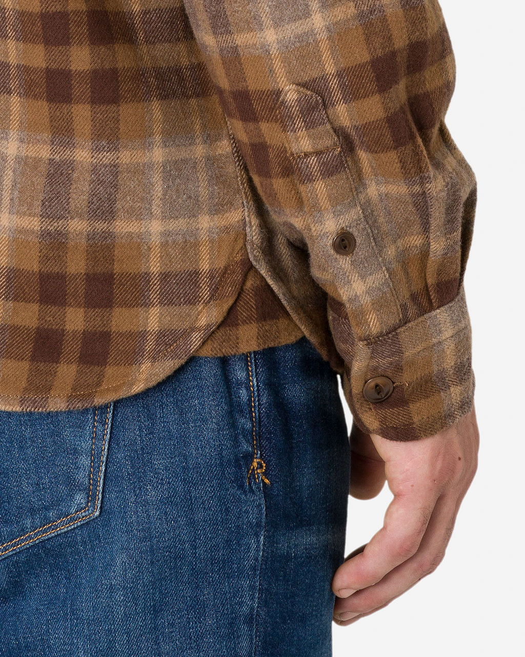 Close-up of a man wearing a Flannel - Utility Shirt - Desert Bark with a brown and beige plaid shirt with buttoned cuffs and blue jeans. The shirt is untucked, and the person's hand is visible on his right side.