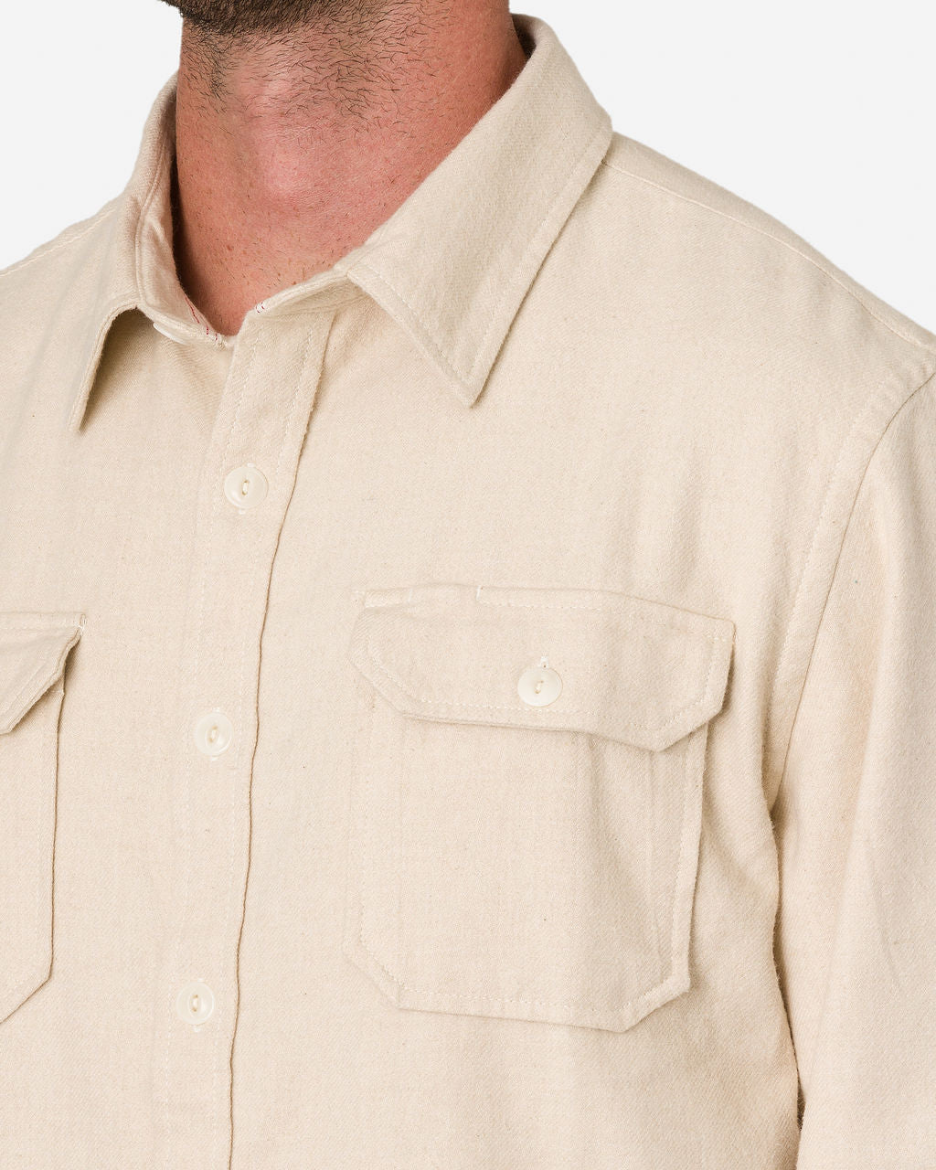 Close-up of a man wearing an Ace Rivington Flannel Ecru color utility button-up shirt with two chest pockets, each with a flap secured by a button. The shirt has a collar and buttoned cuffs. The focus is on the upper torso, showcasing the shirt's design and details.