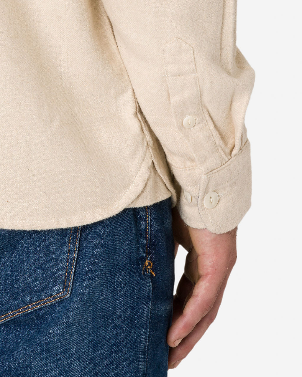 Close-up image of a man wearing an Ecru Flannel - Utility long-sleeve shirt paired with blue jeans by Ace Rivington. The shirt features buttoned cuffs and a curved hem. The person's hand is visible, resting by his side.