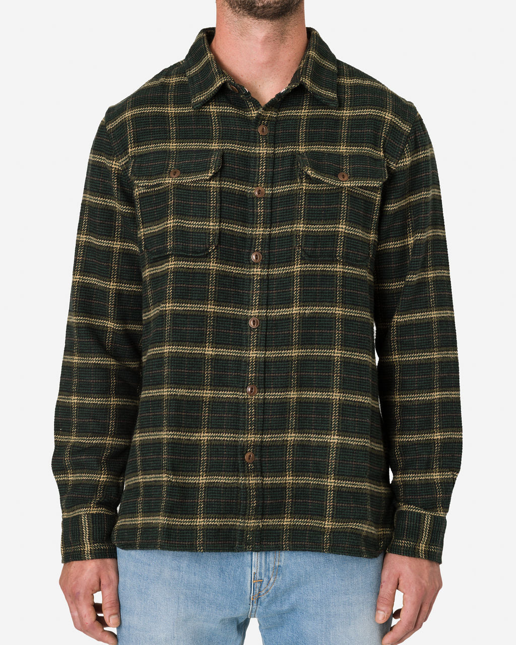 A man is shown focusing on his upper body, emphasizing the design, pattern, and fabric texture of his shirt. He is wearing a Forest Hound long-sleeved button-up flannel utility shirt in a black and brown plaid pattern paired with light blue jeans by Ace Rivington. The shirt features two chest pockets with buttoned flaps, adding a functional detail to its design.