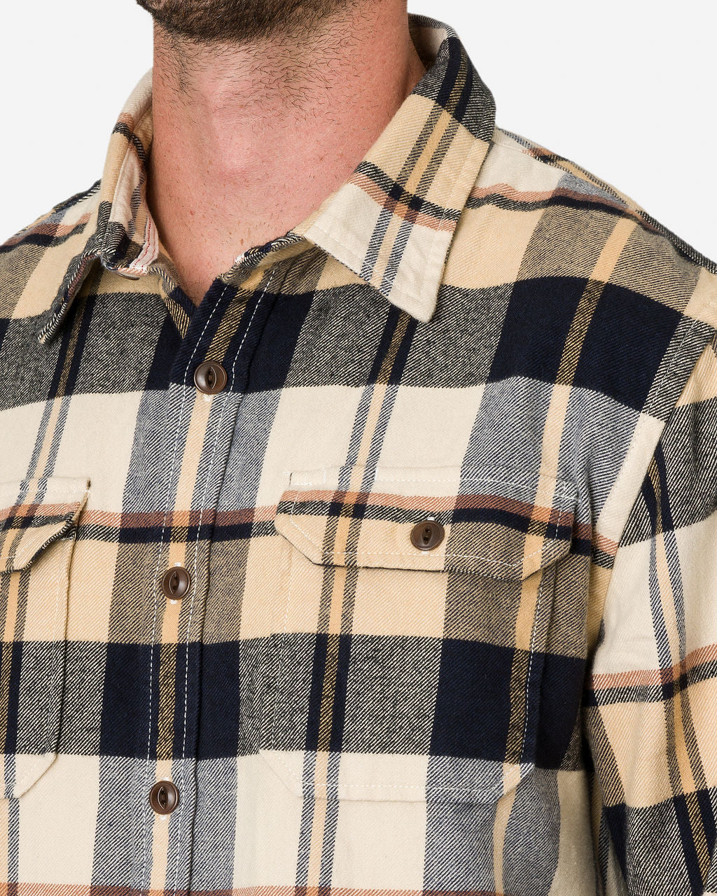 Close-up of a man wearing a midnight dune-flannel utility shirt with a beige, black, gray, and yellow checkered pattern. The shirt has a collar, a button-down front, and two chest pockets with buttoned flaps.