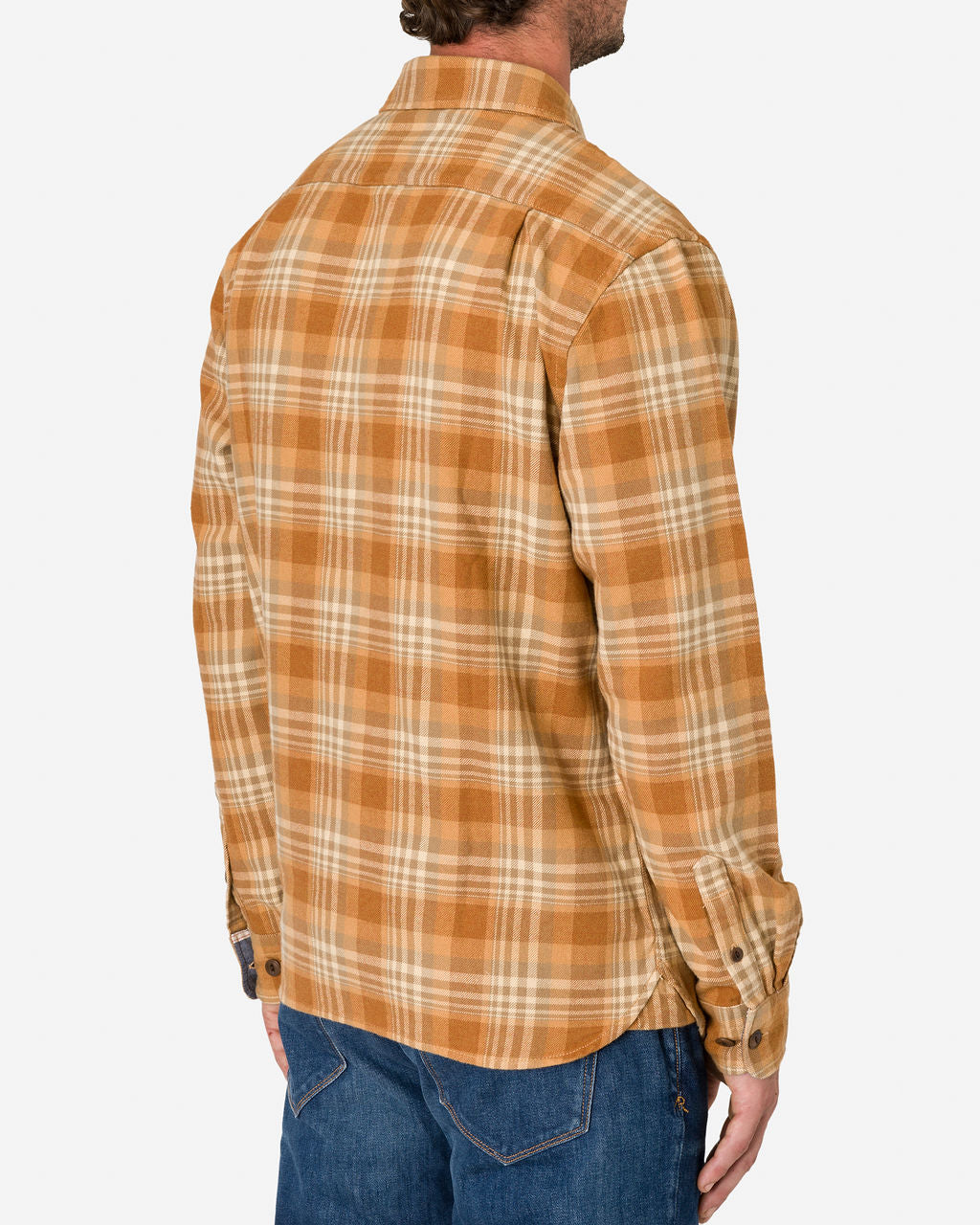 Man wearing an Ace Rivington long-sleeve, button-up flannel utility shirt—sand storm color with a plaid pattern in shades of brown, orange, and beige paired with blue jeans. The man is facing sideways from the camera, showing the right back of the shirt with the collar and buttoned cuffs. 