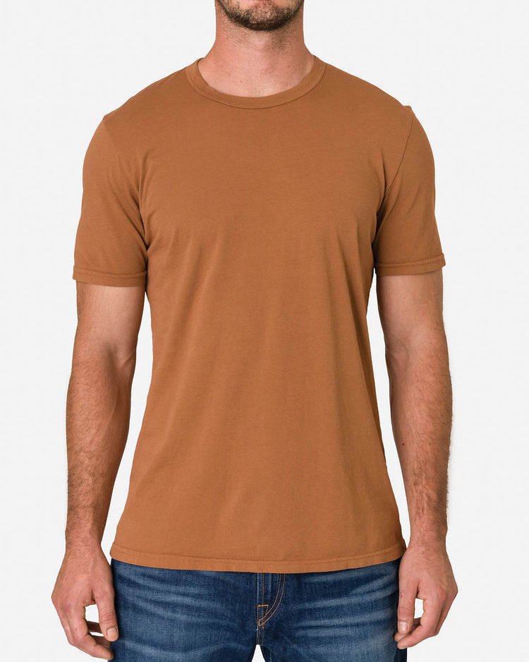 A man wearing an Ace Rivington Super Soft Supima Cotton Tee - Sienna with blue jeans focuses on the upper body. The t-shirt is short-sleeved with a crew neck, fitting comfortably and showcasing its soft, high-quality Supima cotton fabric highlighting the design and fit of the t-shirt.