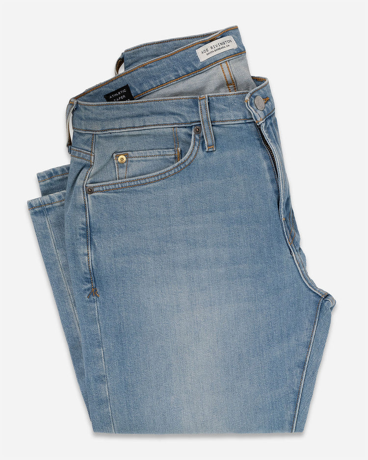 A pair of Athletic Taper Denim Jeans - Light Vintage folded neatly, showing the front pockets, belt loops, and button closure. 