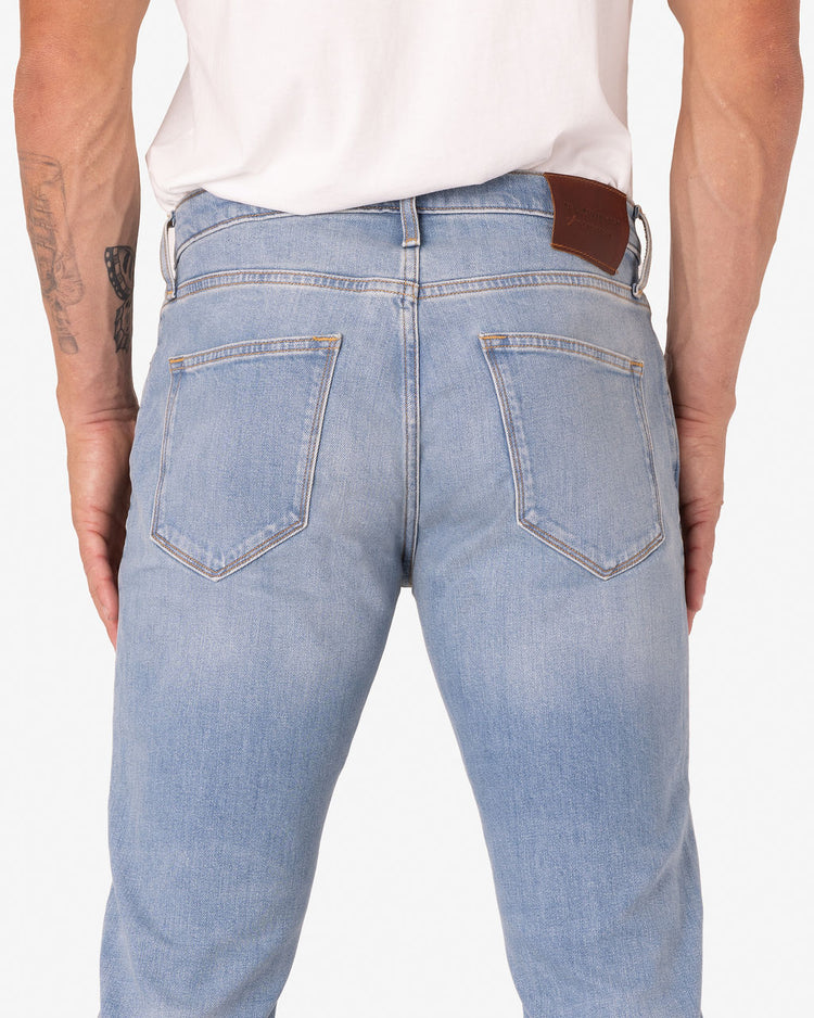 Back view of a man wearing Athletic Taper Denim Jeans - Light Vintage
 and a white shirt. The jeans have two back pockets and a brown leather patch on the waistband.