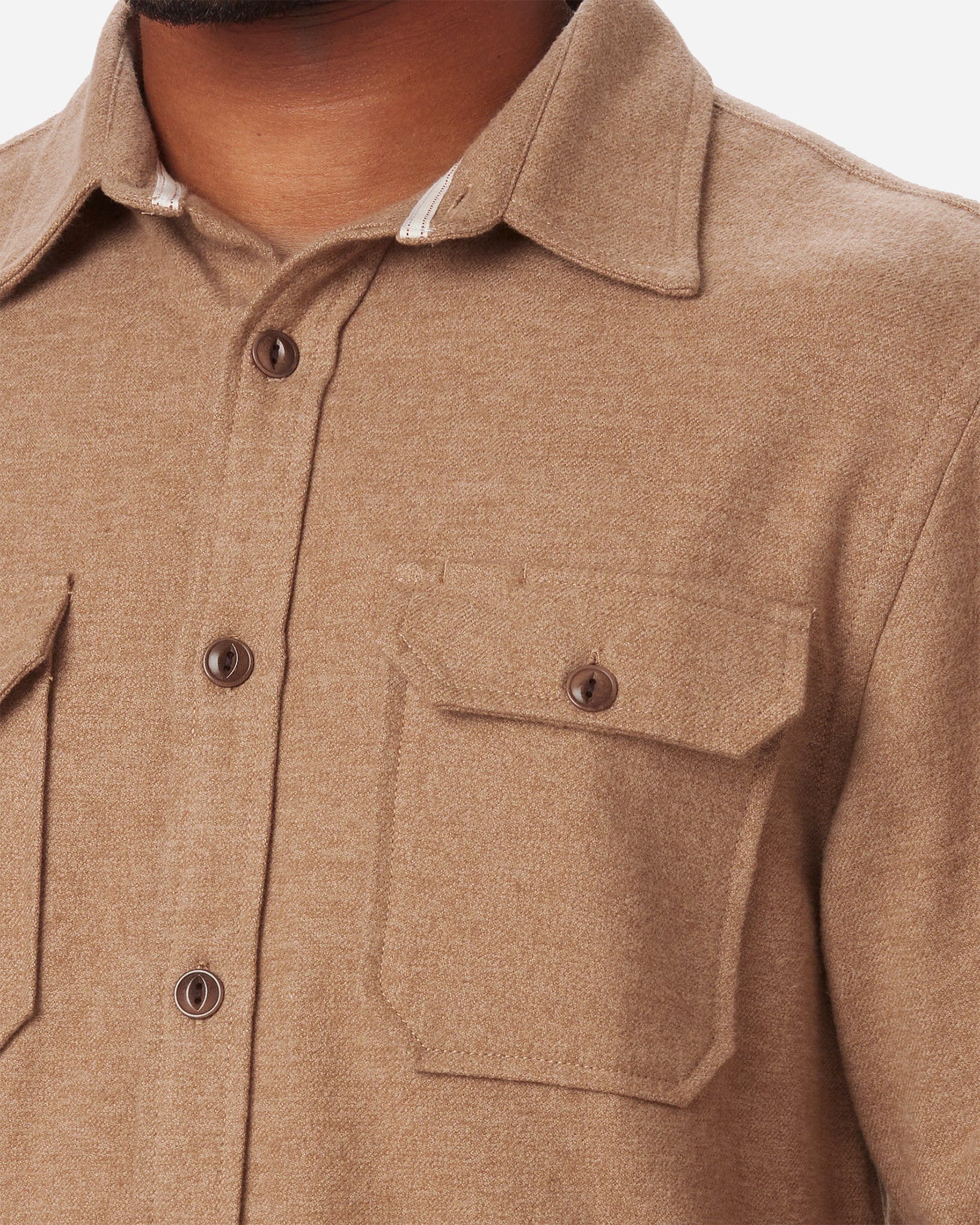 Close-up of a man wearing an Ace Rivington camel-colored flannel utility H1 shirt with two chest pockets, each secured with a buttoned flap. The shirt features a collar and visible stitching details.