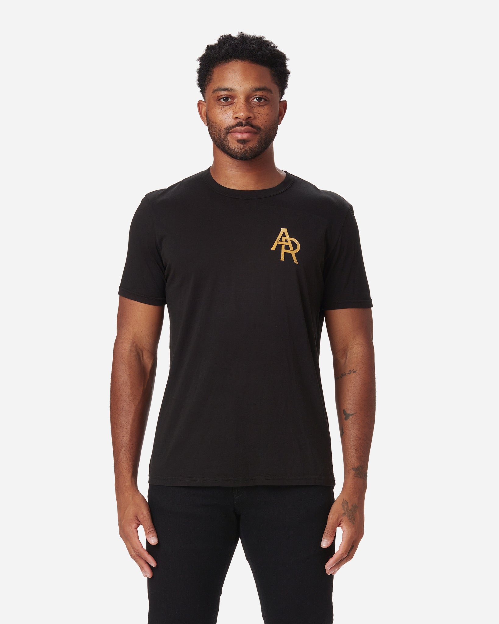 Man wearing a black Ace Rivington Supima Tee Crewneck short sleeves Vintage Flyer t-shirt. Features a small, gold 'AR' logo on the left chest. The image highlights the fit and design of the t-shirt, making it relevant for showcasing the product's style and branding on a plain white background.