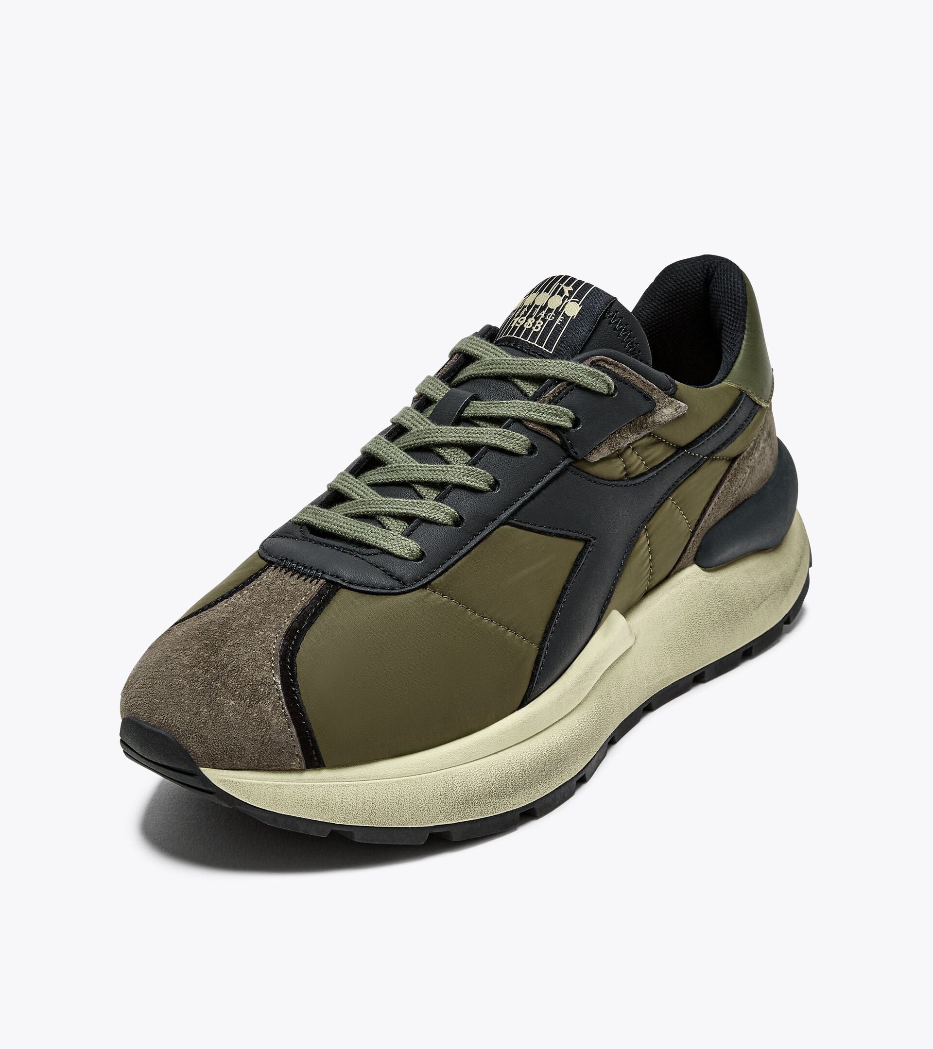 Left-pair angled front view of the Ace Rivington Diadora - Mercury Elite - Beech Green, showcasing its retro-inspired design with a blend of textile and leather materials, waxed cotton laces, and an EVA midsole. The olive green and brown tones highlight the 1970s track shoe aesthetic.