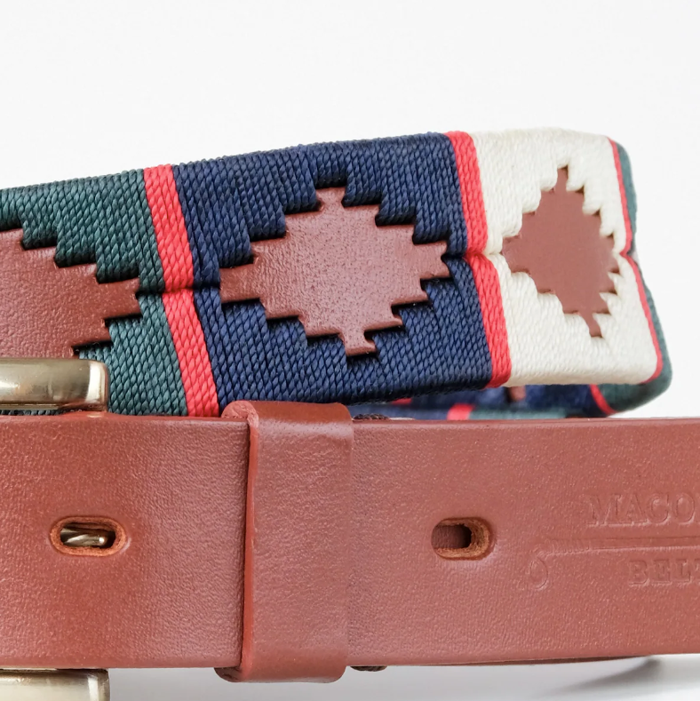 Close-up of the Ace Rivington Macondo Belt - Alpino. This belt features an intricate woven pattern with geometric shapes in navy blue, green, and white, separated by red vertical stripes. It has a brown leather strap with visible stitching and a brass buckle. The brand name, 'MACONDO BELT,' is partially embossed on the leather.