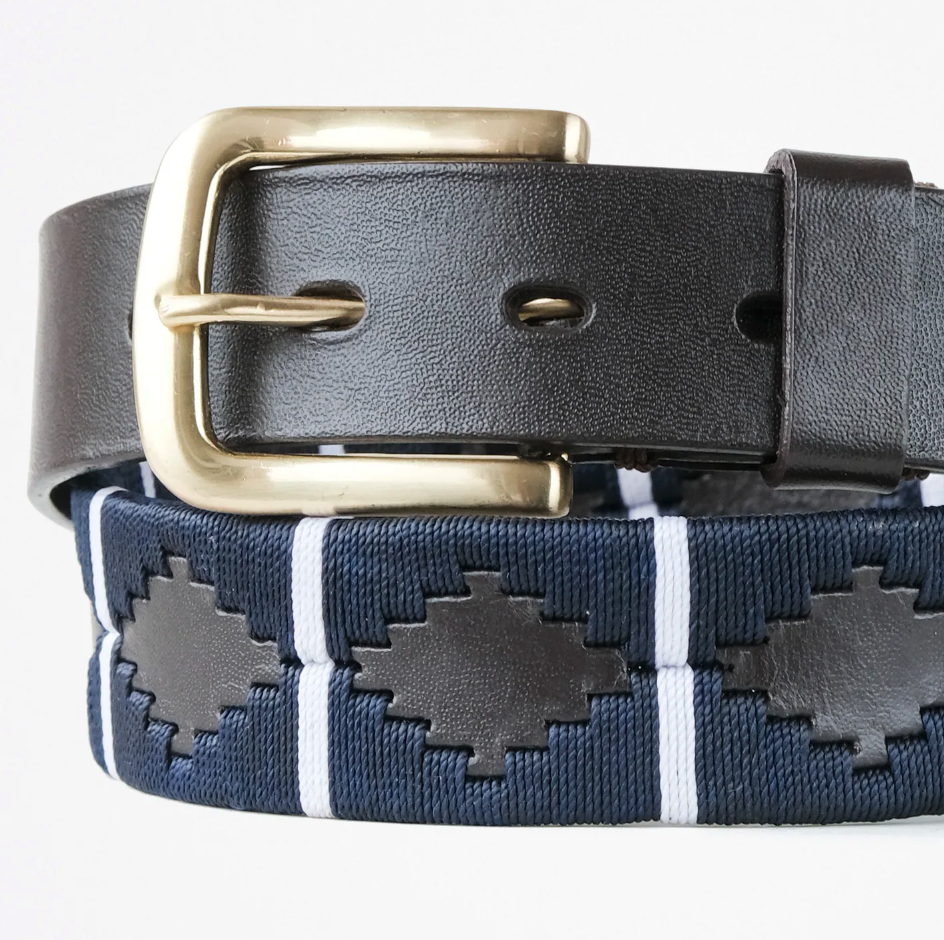 Close-up of the Ace Rivington Macondo Belt - Bandolero. This belt features a woven pattern with geometric shapes in navy blue and black, separated by white vertical stripes. It has a black leather strap with a smooth finish and a brass buckle. The belt showcases a blend of traditional and modern design elements, making it both stylish and versatile.