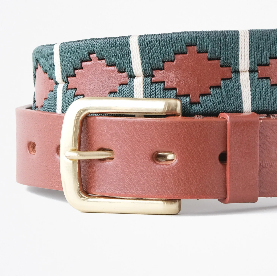 Close-up of the Ace Rivington Macondo Belt - Cazador. This belt features an intricate woven pattern with geometric shapes in brown and green, separated by white vertical stripes. It has a brown leather strap with a gold buckle. The combination of the rich leather and colorful woven fabric creates a stylish and eye-catching accessory.