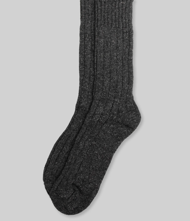 A pair of Ace Rivington Wool Silk Boot Sock - Charcoal features a ribbed texture, highlighting its thickness and warmth, suitable for cold weather. The material looks soft and comfortable, showcasing a blend of wool and silk for warmth and a smooth feel. The sock is displayed against a plain gray background, emphasizing its sophisticated design.