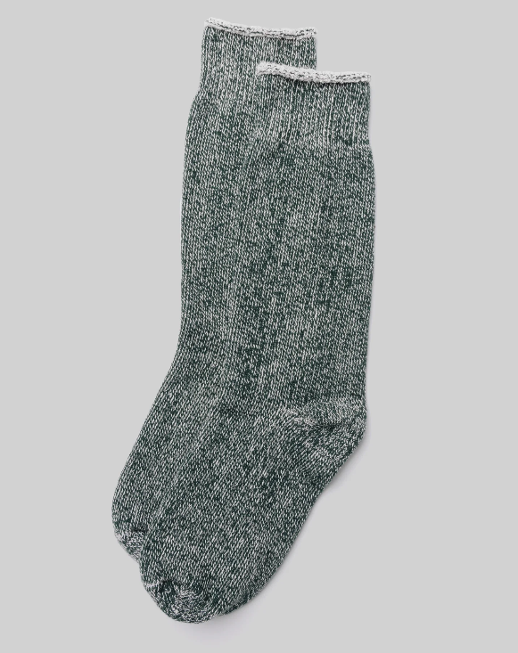 A pair of Ace Rivington The Sunday Socks - Bottle Green, displayed on a plain background features a thick, cozy knit texture with ribbed cuffs. The marled effect of the fabric comes from the blend of green and white threads. One sock slightly overlaps the other, highlighting their comfortable and warm design, perfect for casual or lounging wear.