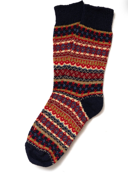 A pair of Ace Rivington American Trench Cotton Fair Isle Sock features a vibrant Fair Isle pattern with colors including red, navy blue, mustard yellow, and beige. The pattern consists of intricate geometric designs and stripes, creating a visually appealing and traditional look. The toe, heel, and cuff of the sock are solid navy blue, providing a contrast to the colorful pattern.