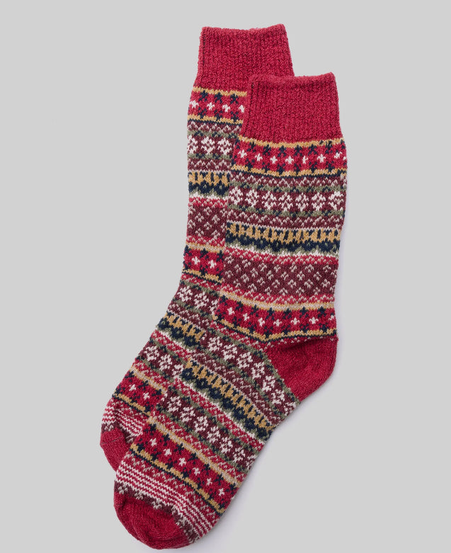 A pair of Ace Rivington American Trench Cotton Fair Isle Socks, featuring a vibrant and intricate pattern with red, white, yellow, and blue geometric shapes and motifs. The socks have a red heel, toe, and cuff, contrasting with the detailed design. The background is light gray, emphasizing the festive and traditional appearance of the socks.