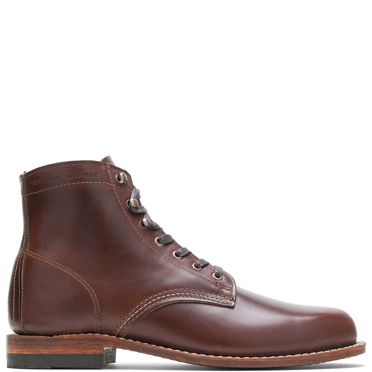 Ace Rivington Wolverine - 1000 Mile - Plain Toe Original brown boot leather features a sleek design with a plain toe, metal eyelets for laces, and detailed stitching along the sides and heel. The sole is made of wood and rubber, providing durability and a classic look.