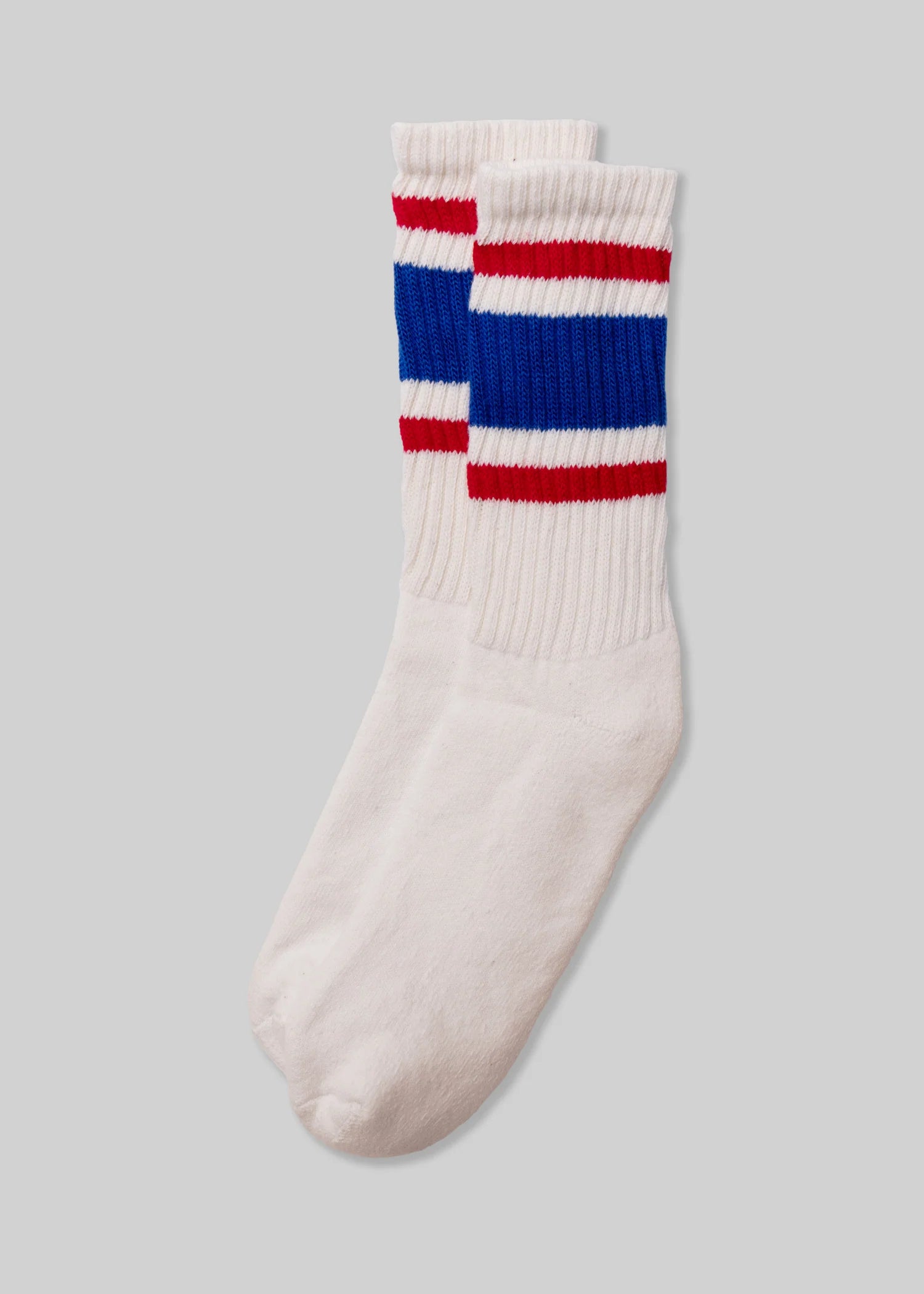 A pair of Ace Rivington American Trench Retro Stripe white socks with a ribbed upper section featuring retro stripes in red and blue. The design is reminiscent of vintage athletic socks, adding a nostalgic and stylish touch.