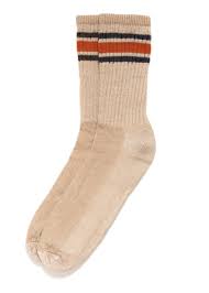 A pair of peach-colored American Trench Merino Activity Socks features a ribbed texture along the upper portion and three horizontal stripes near the top in orange, and green. The sock is made of a soft, comfortable material, likely merino wool, known for its moisture-wicking and temperature-regulating properties.