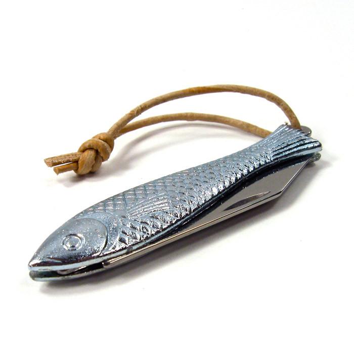 A metallic fish-shaped knife with a textured surface resembling fish scales, featuring a small blade partially visible along the side. The knife has a leather loop attached to the tail end, tied in a knot.